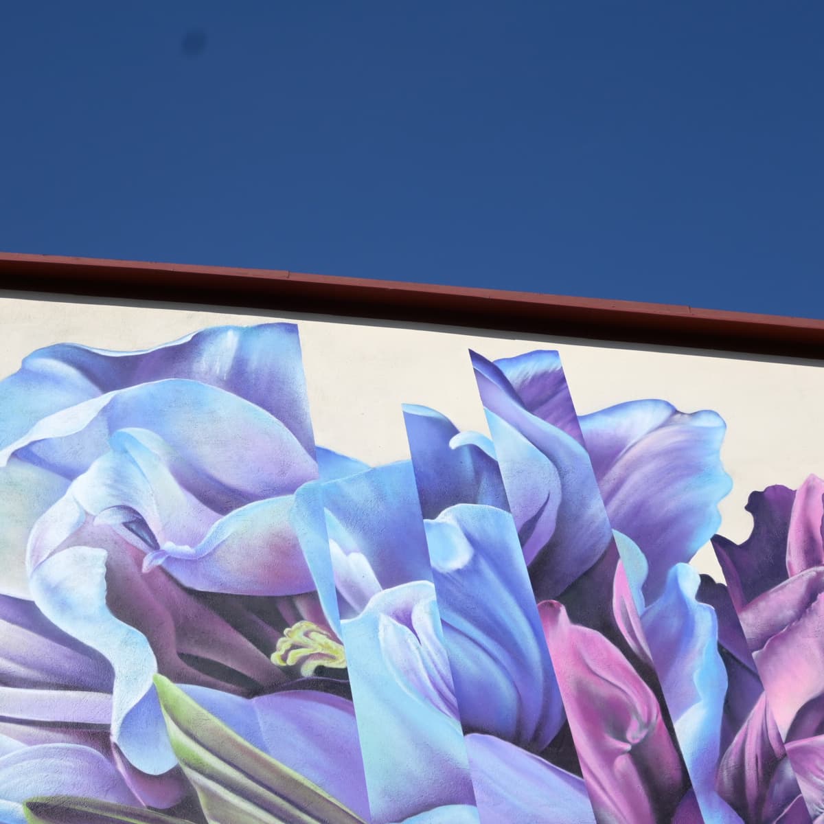 En stor väggmålning av lila blommor på sidan av en byggnad.