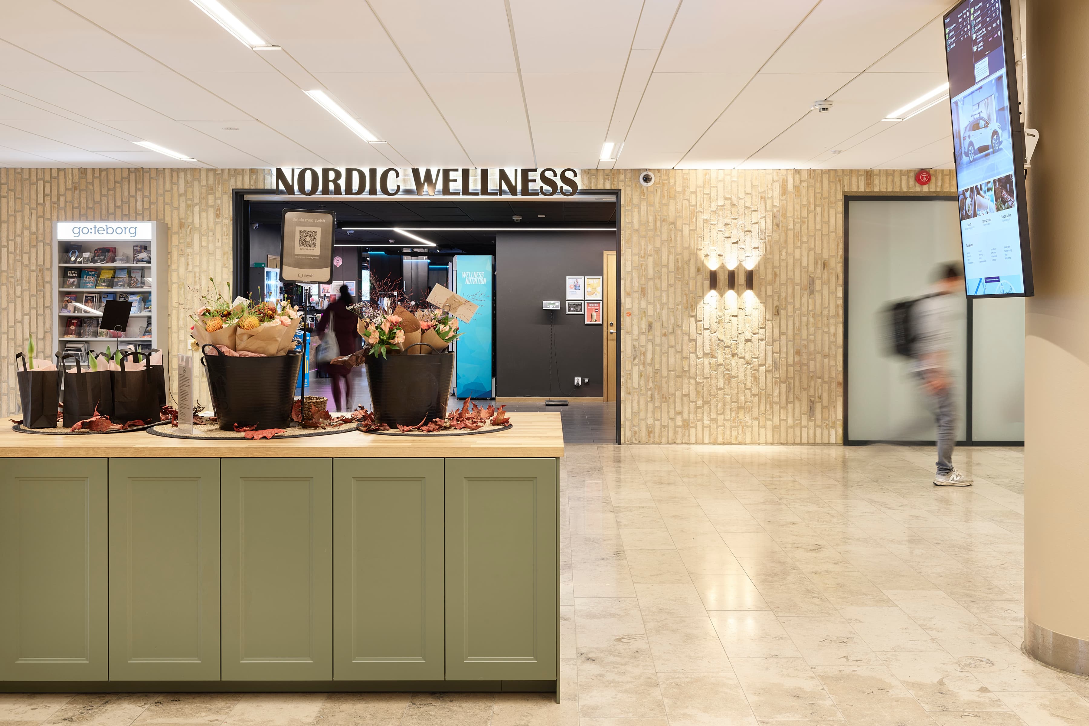 En person som går förbi en butiksfasad med blommor på disken.