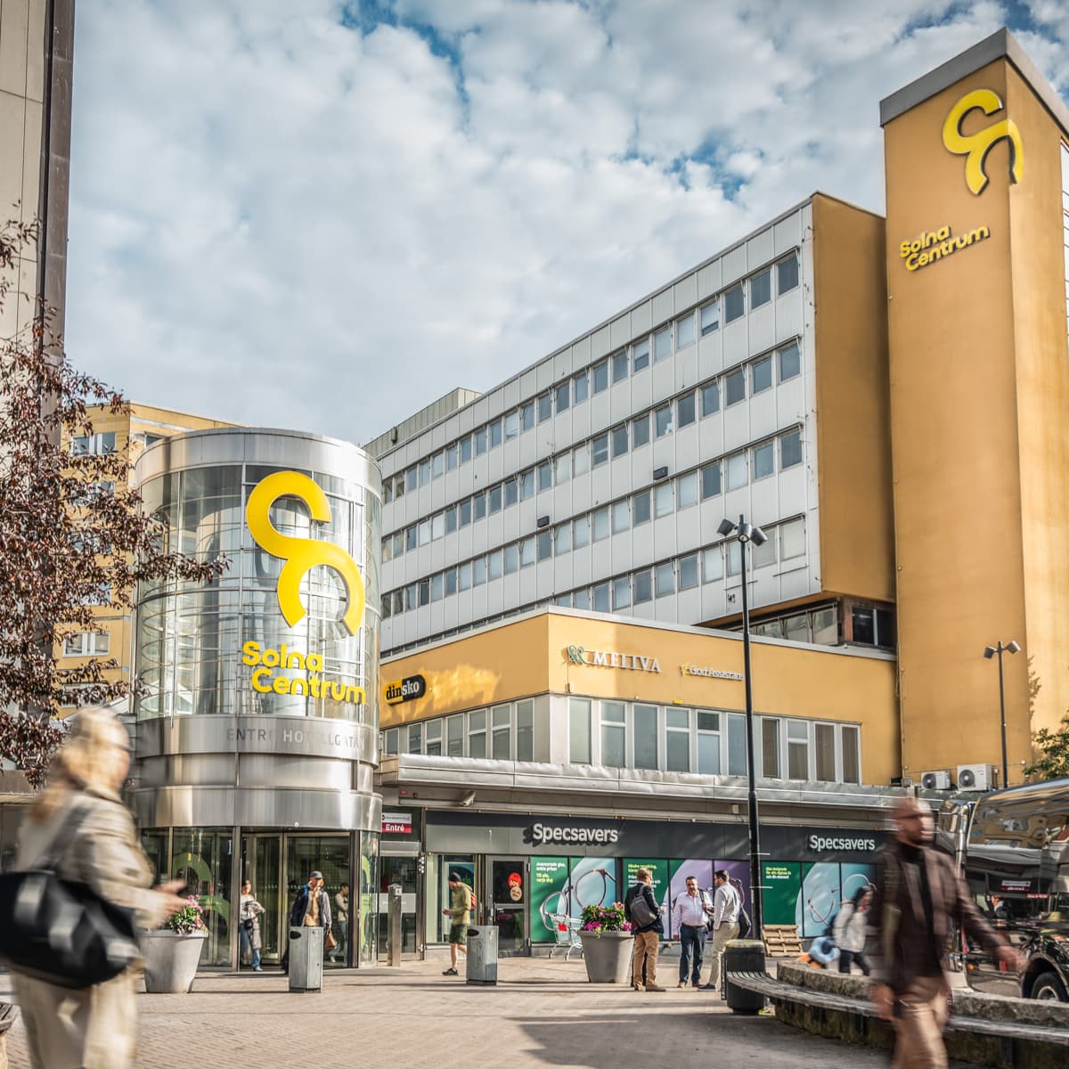 En grupp människor som går längs en gata bredvid höga byggnader.