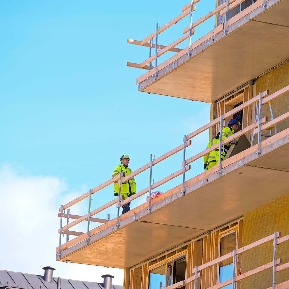 Två byggnadsarbetare står på en balkong på en byggnad.