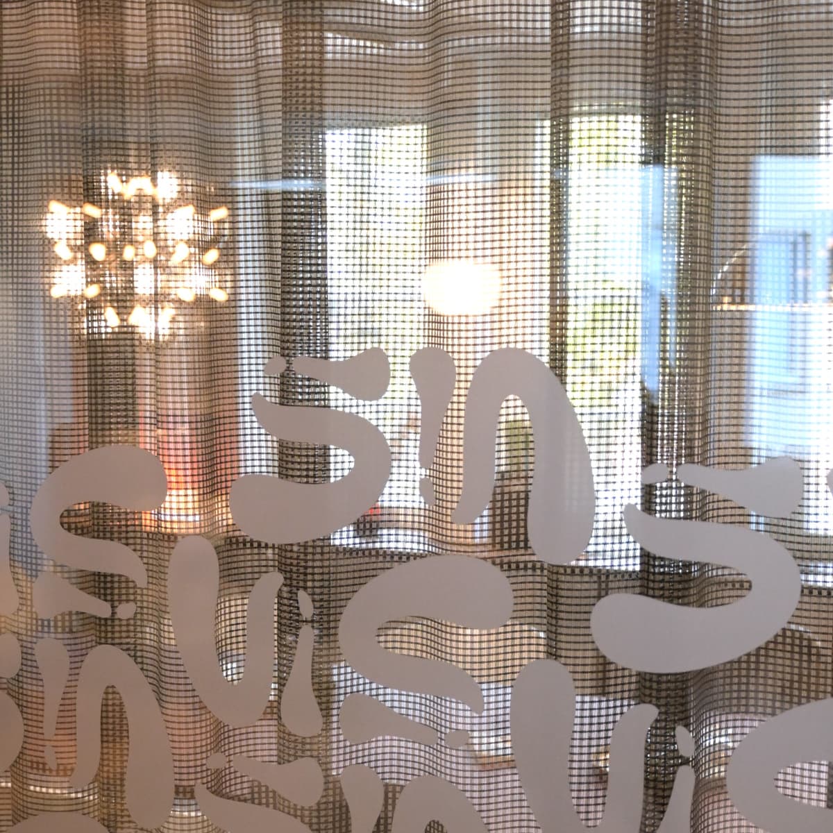 En närbild av ett fönster med en gardin och en ljuskrona.