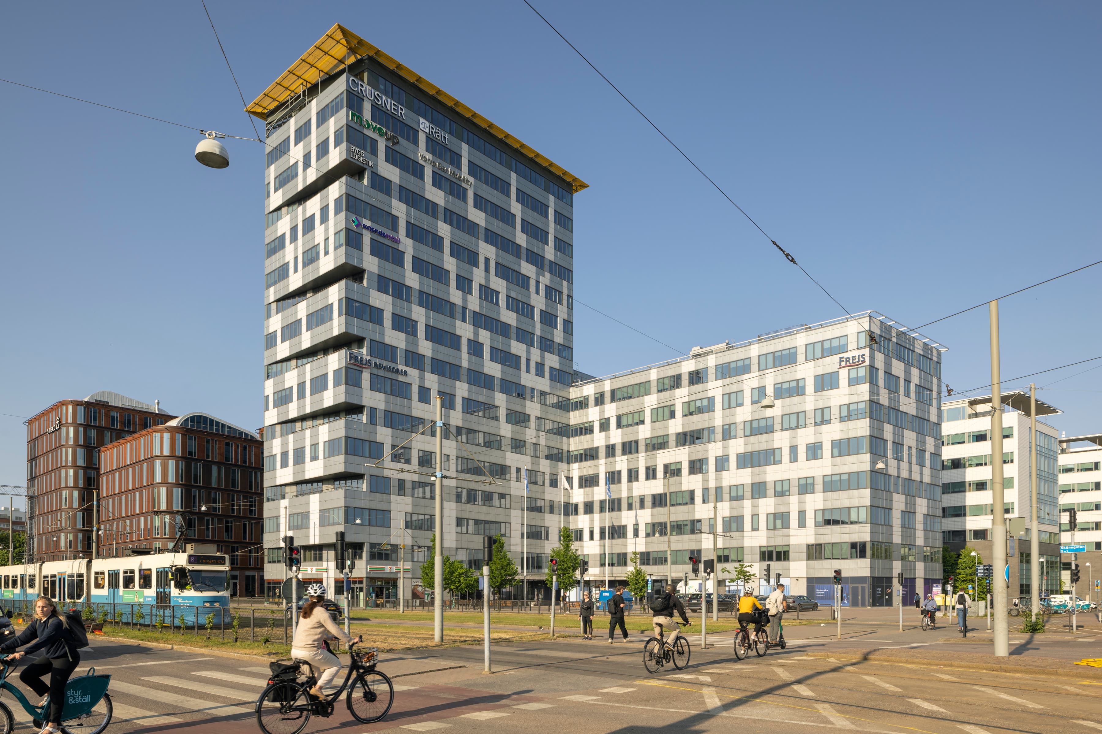 En grupp människor som cyklar längs en gata bredvid höga byggnader.