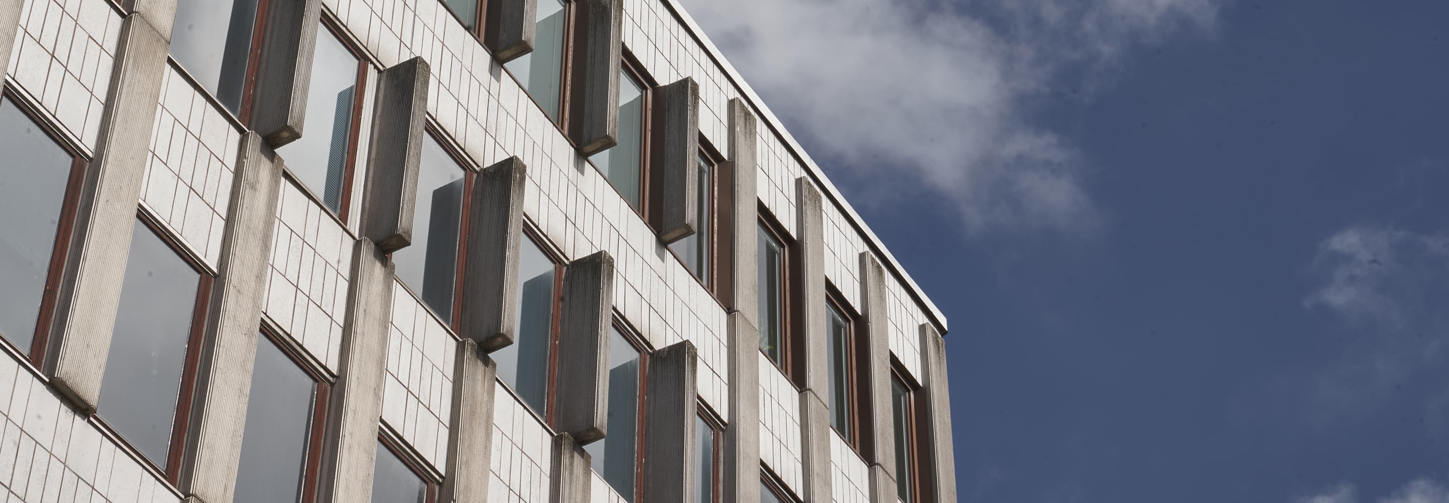 En hög byggnad med massor av fönster under en molnig blå himmel.