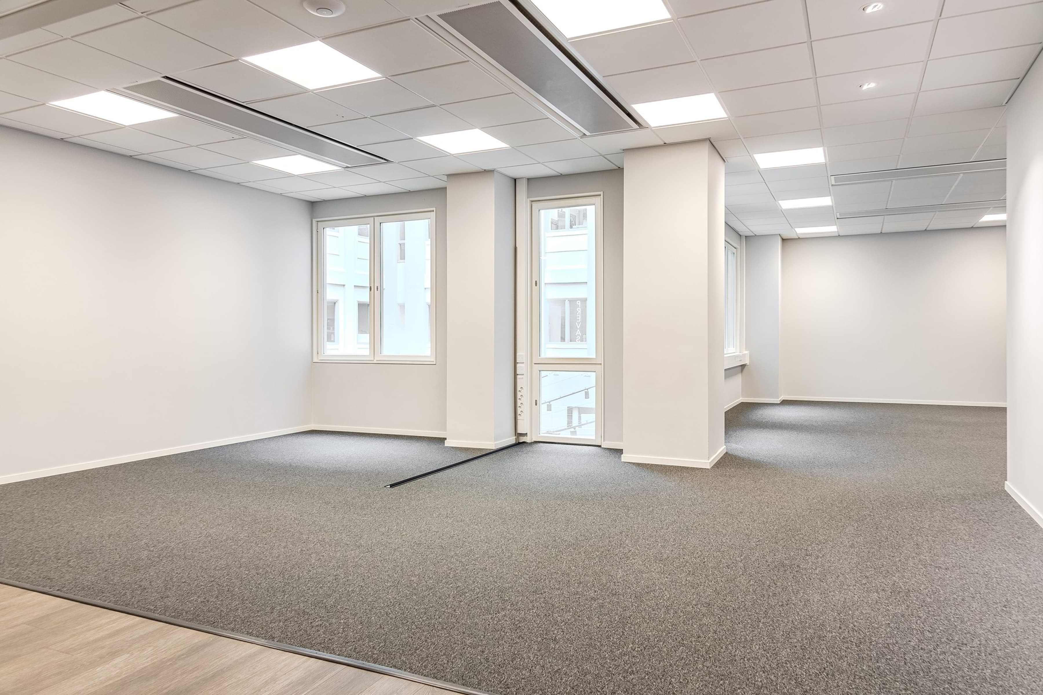 Ett tomt rum med två fönster och en golvmatta.