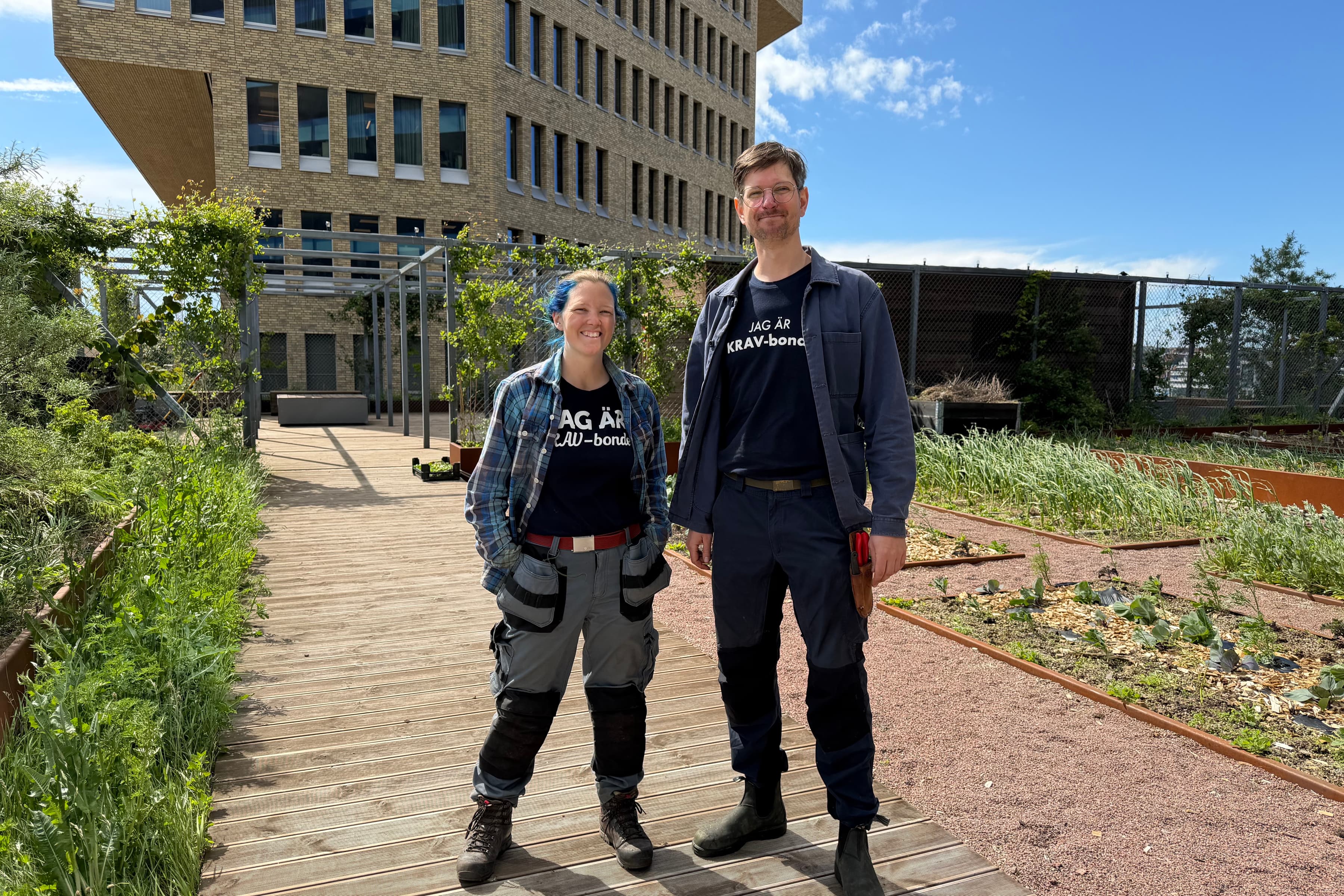 Två personer som står på en träbro framför en byggnad.
