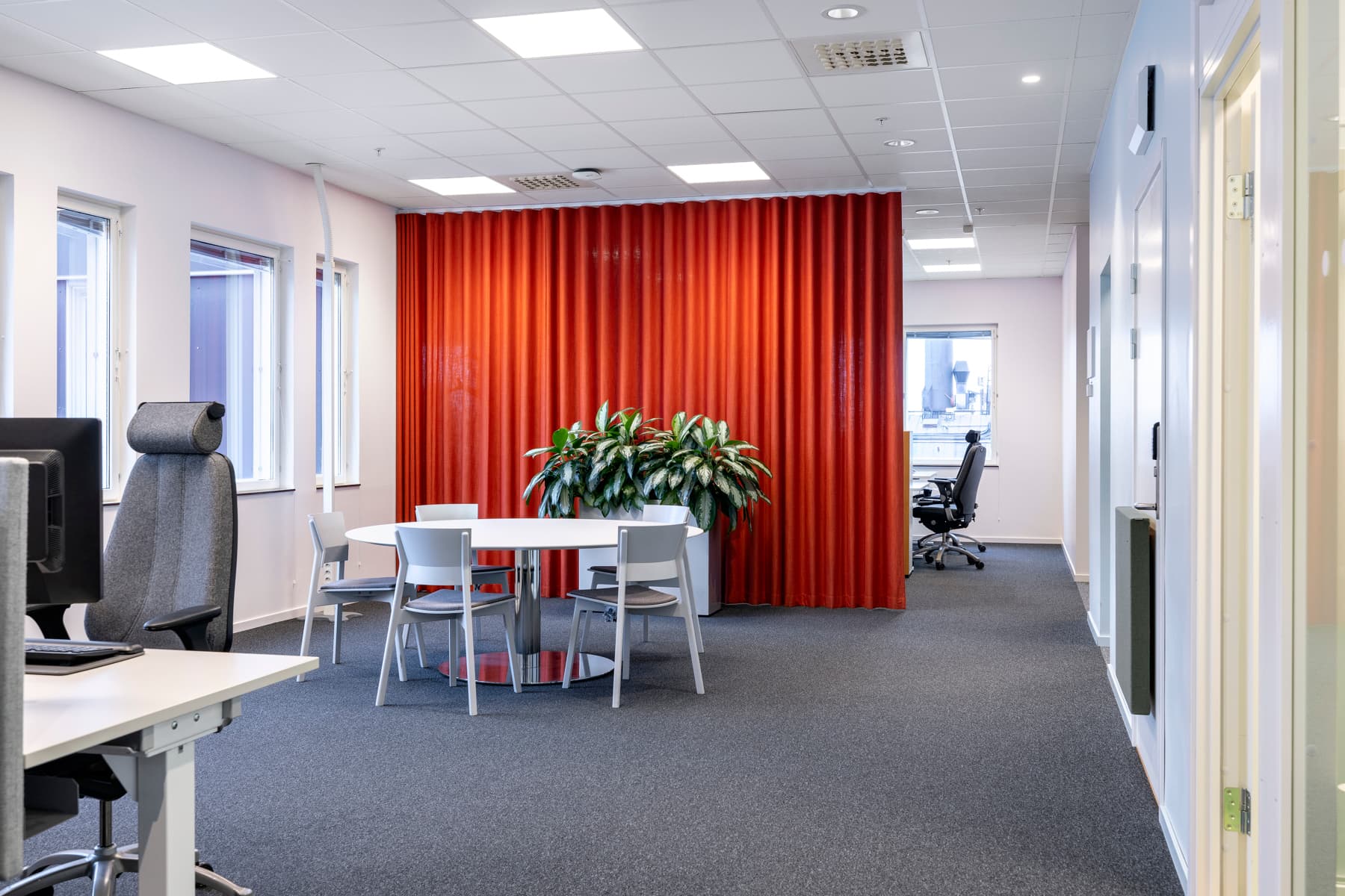 Ett kontor med en röd gardin och ett vitt bord med stolar.