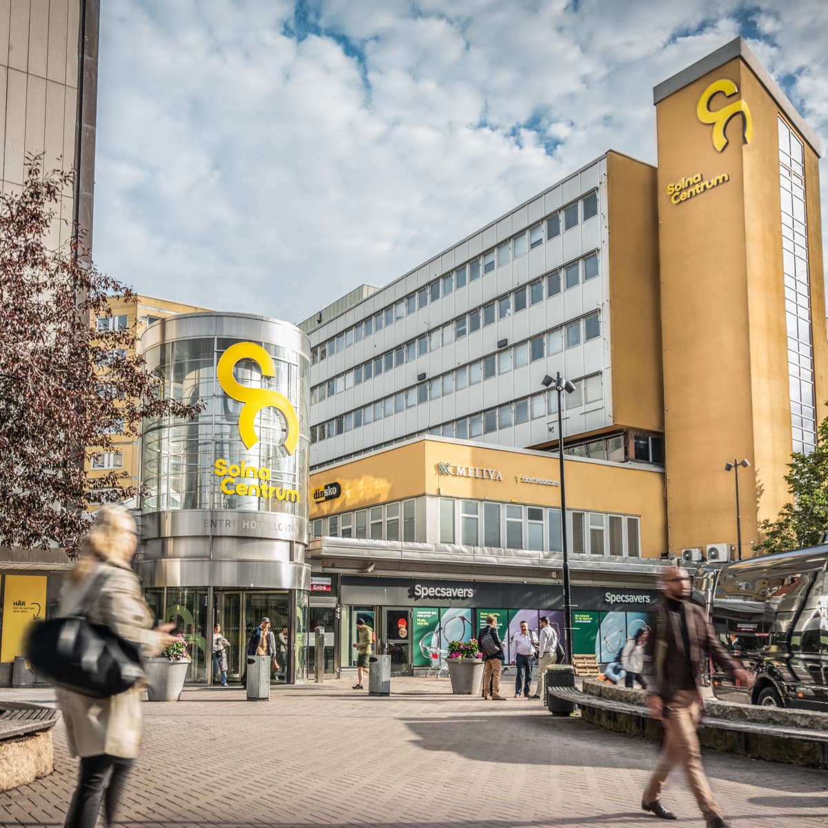 En grupp människor som går längs en gata bredvid höga byggnader.