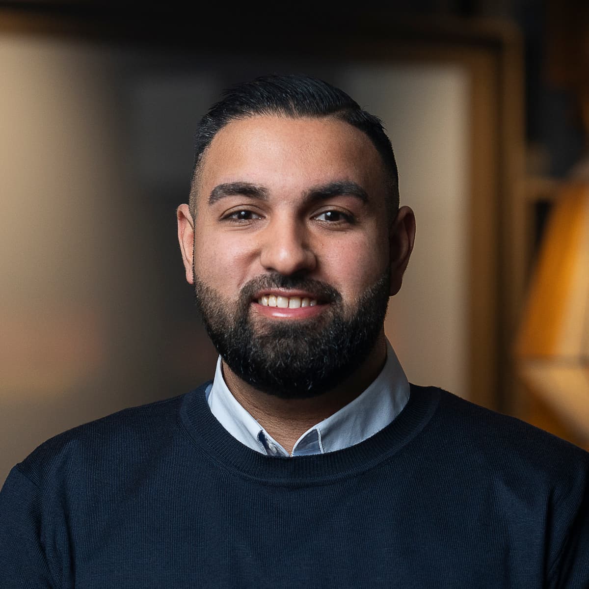 En man med skägg står i ett rum.