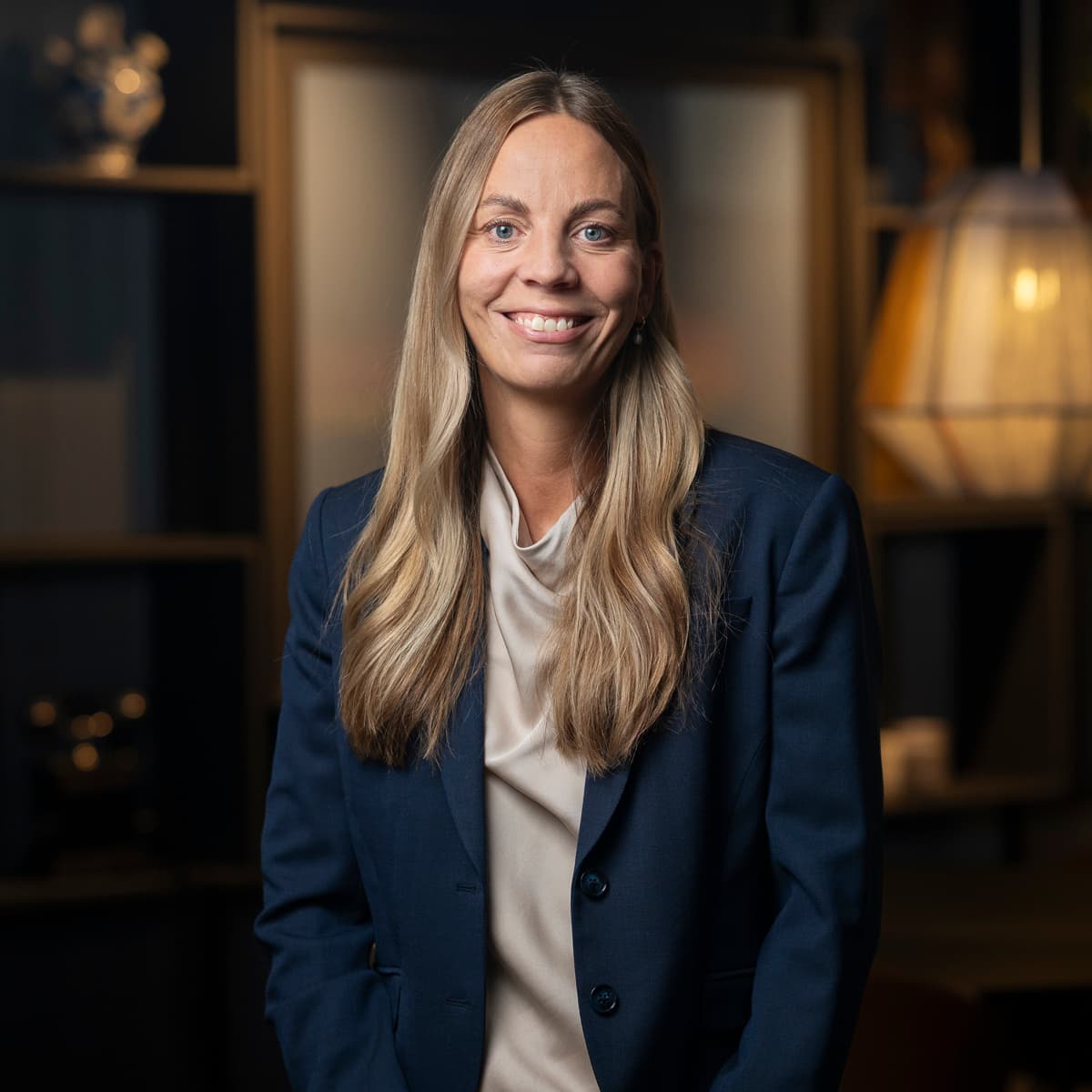 En kvinna står i ett rum med en lampa i bakgrunden.