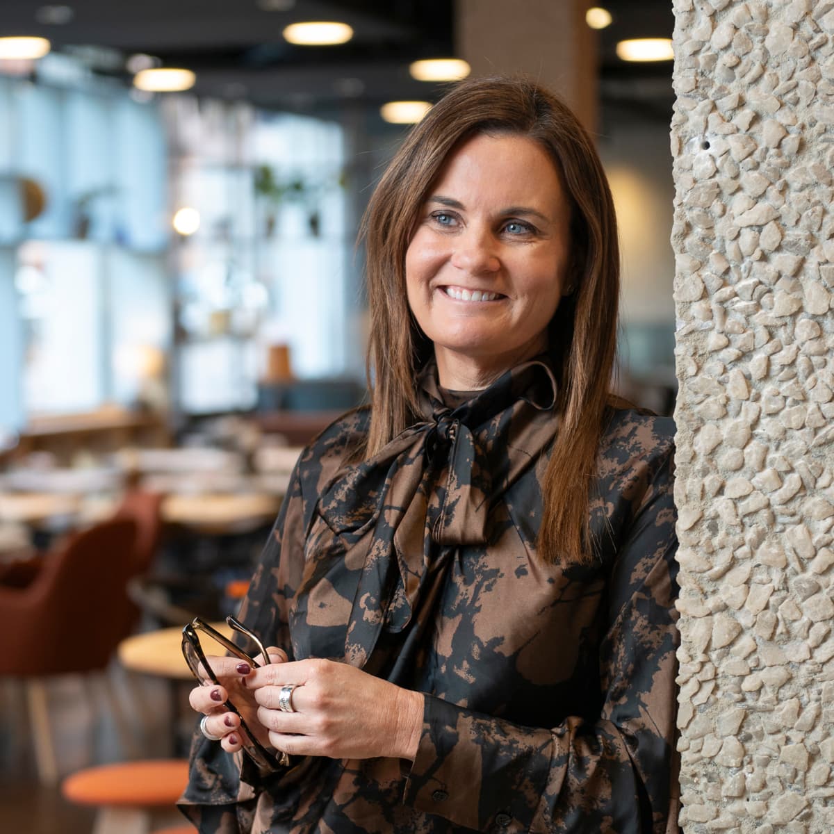 En kvinna står intill en vägg och håller i en mobiltelefon.