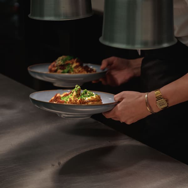 En person som håller i en tallrik med mat i ett kök.