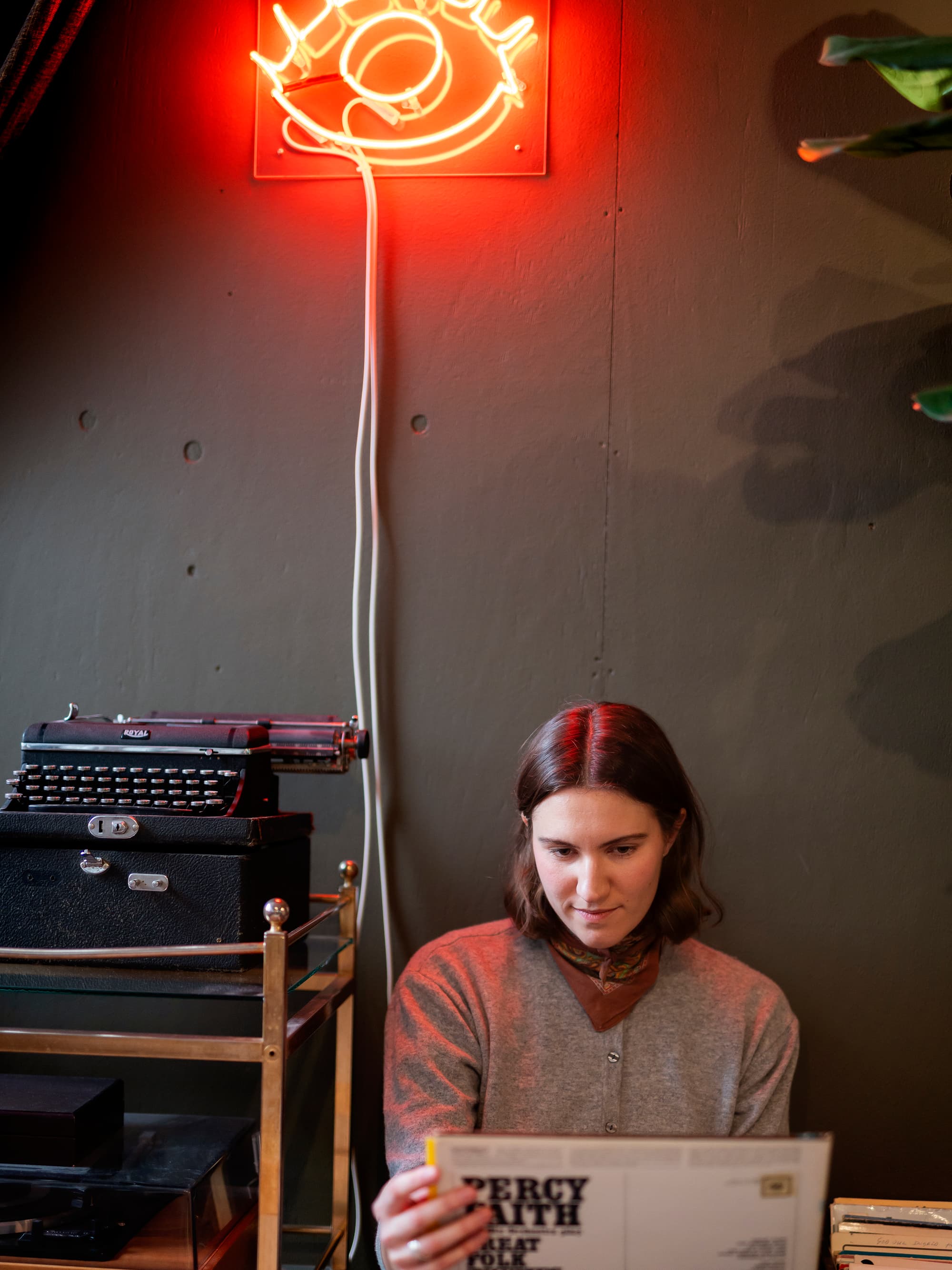 En kvinna sitter framför en neonskylt.