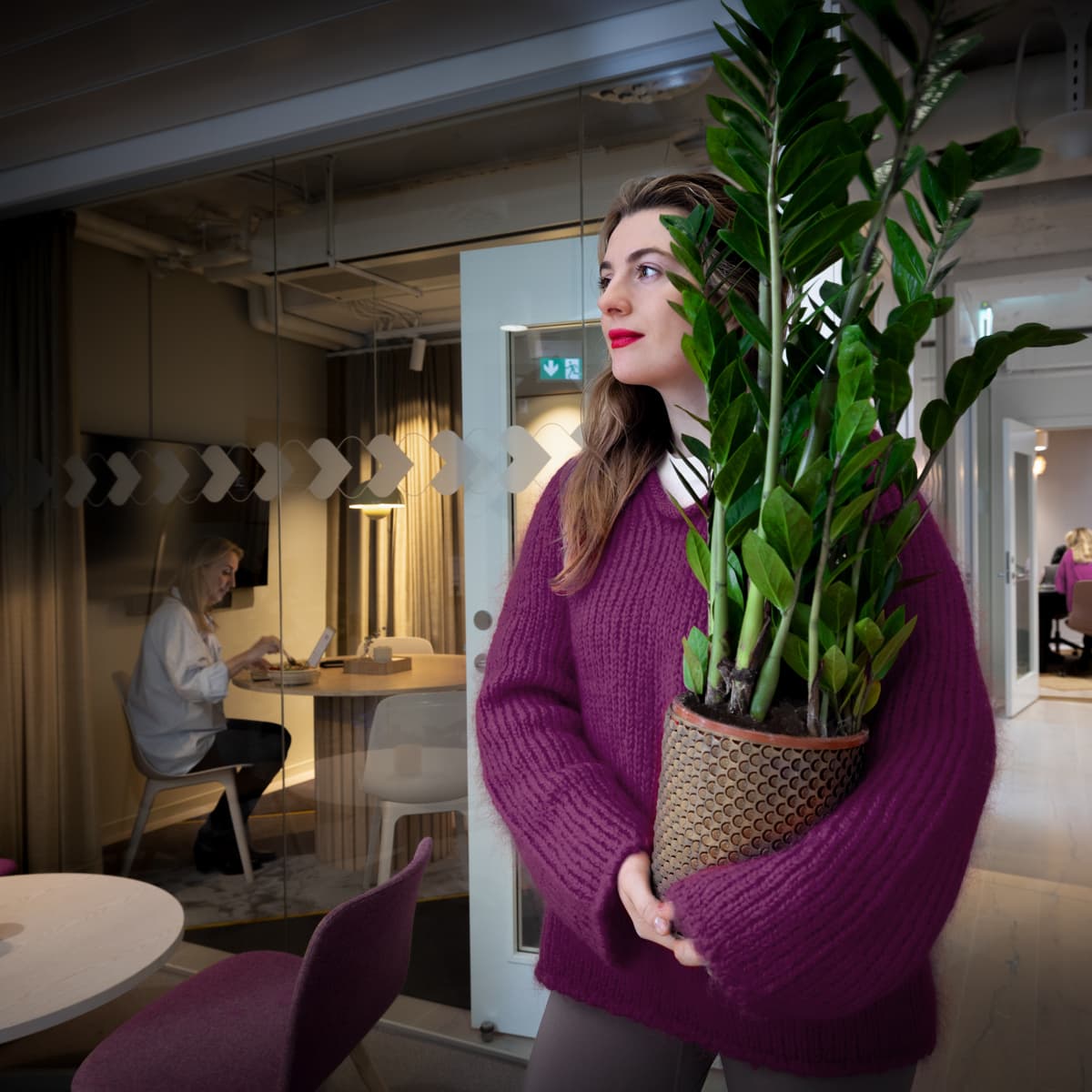 En kvinna håller i en krukväxt på ett kontor.