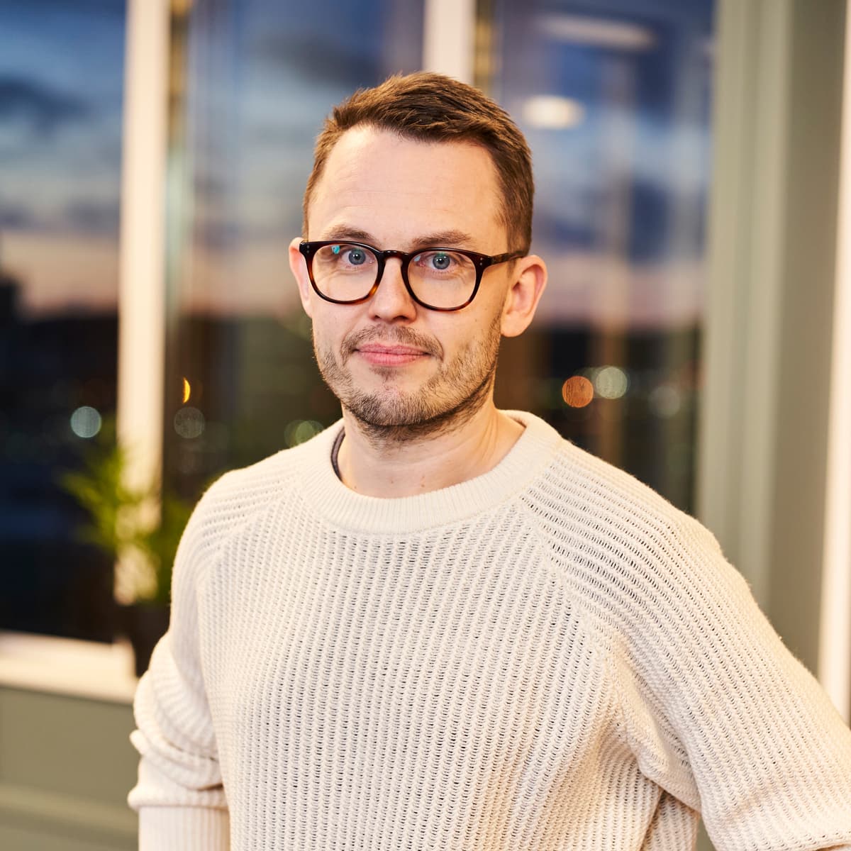 En man med glasögon står framför ett fönster.