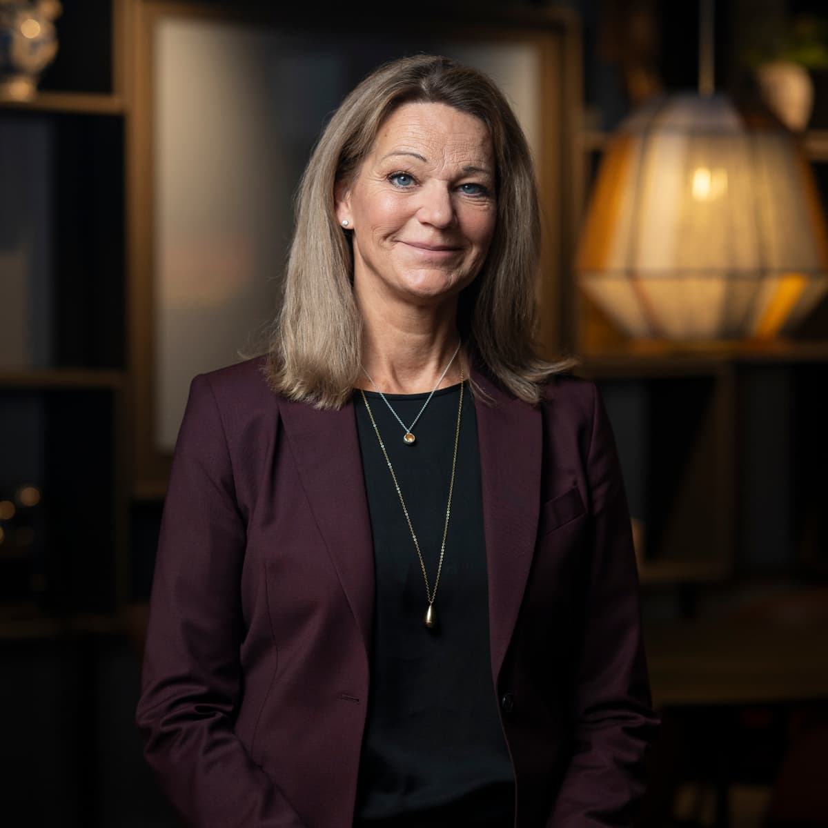 En kvinna i lila jacka står i ett rum.