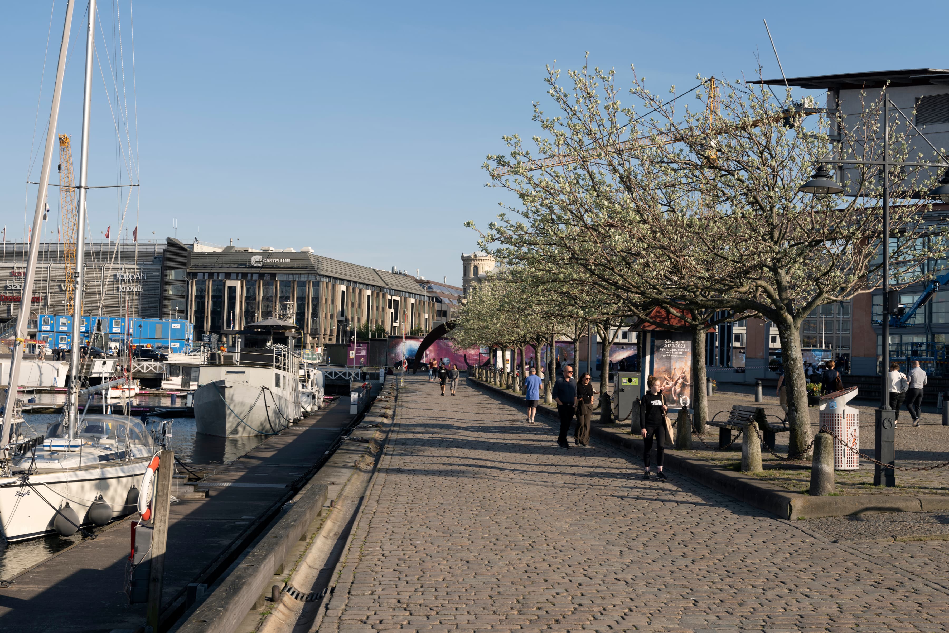 En grupp människor som går på en trottoar bredvid båtar.