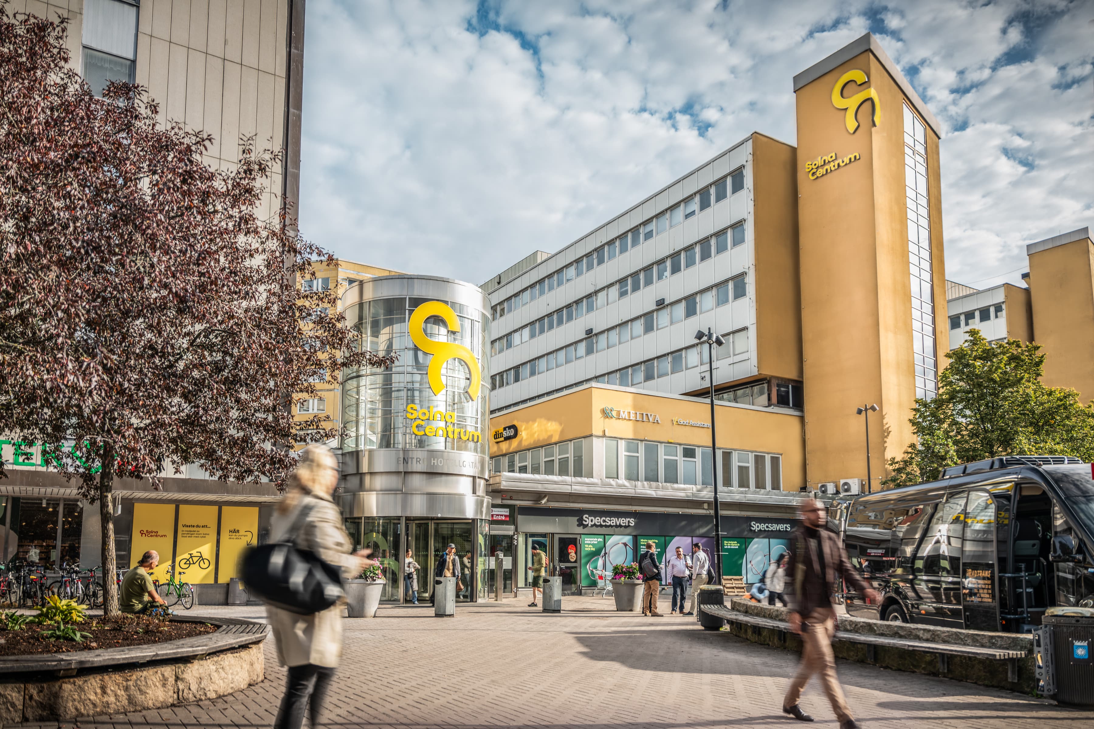 En grupp människor som går längs en gata bredvid höga byggnader.