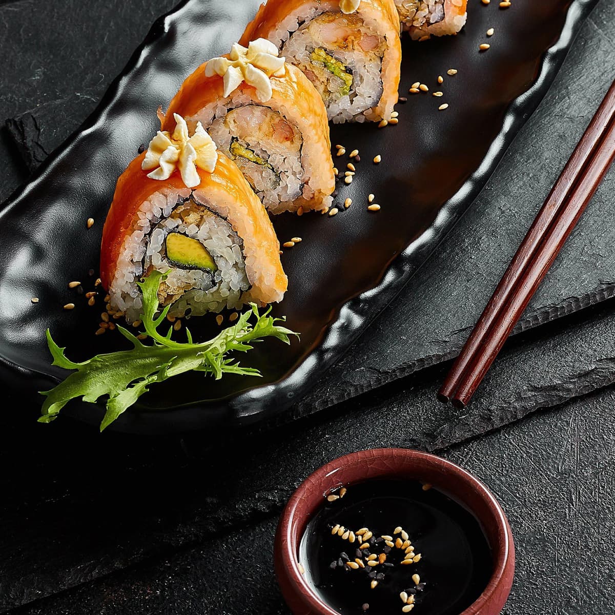 En svart tallrik med sushi och ätpinnar på.