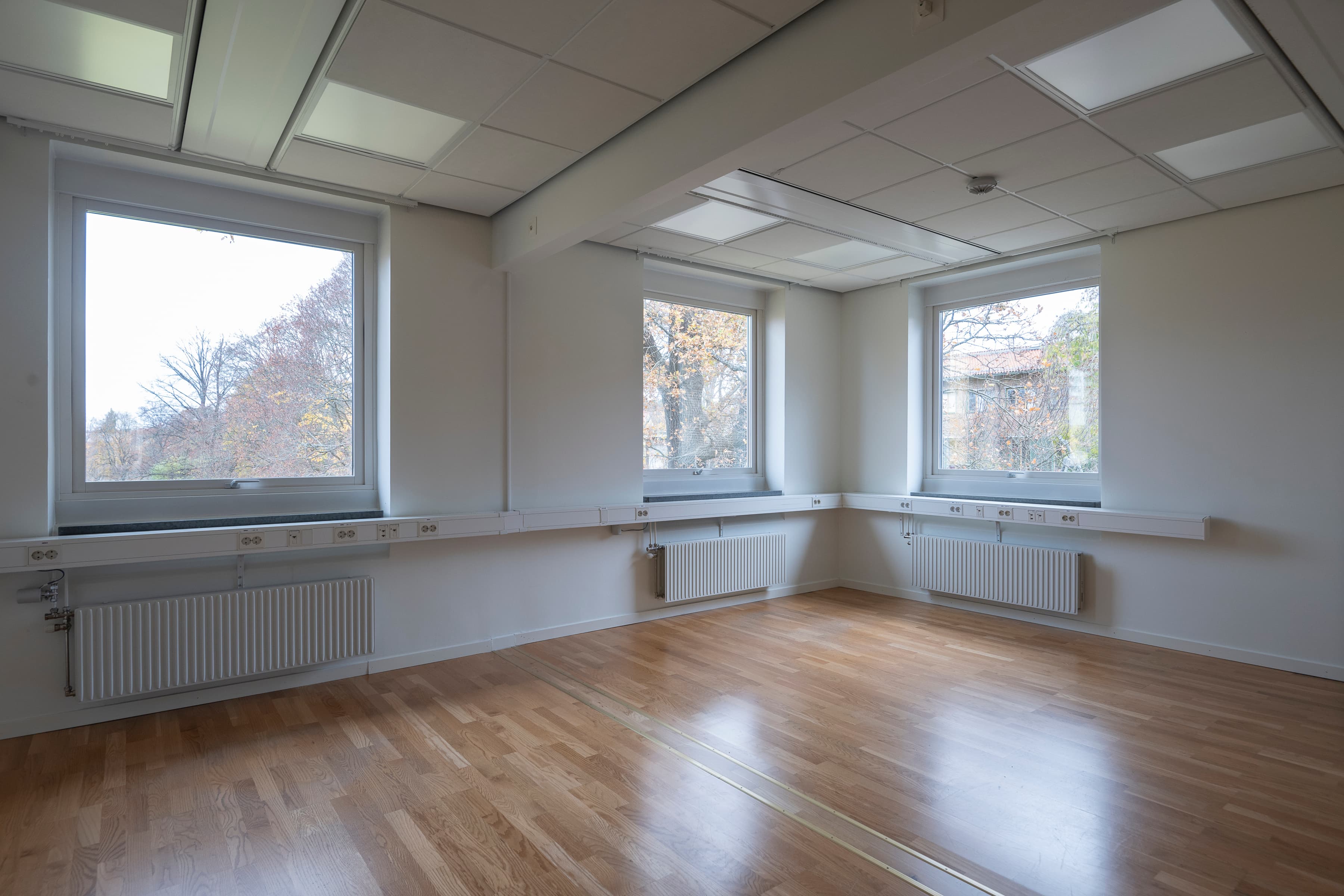 Ett tomt rum med tre fönster och ett hårt trägolv.