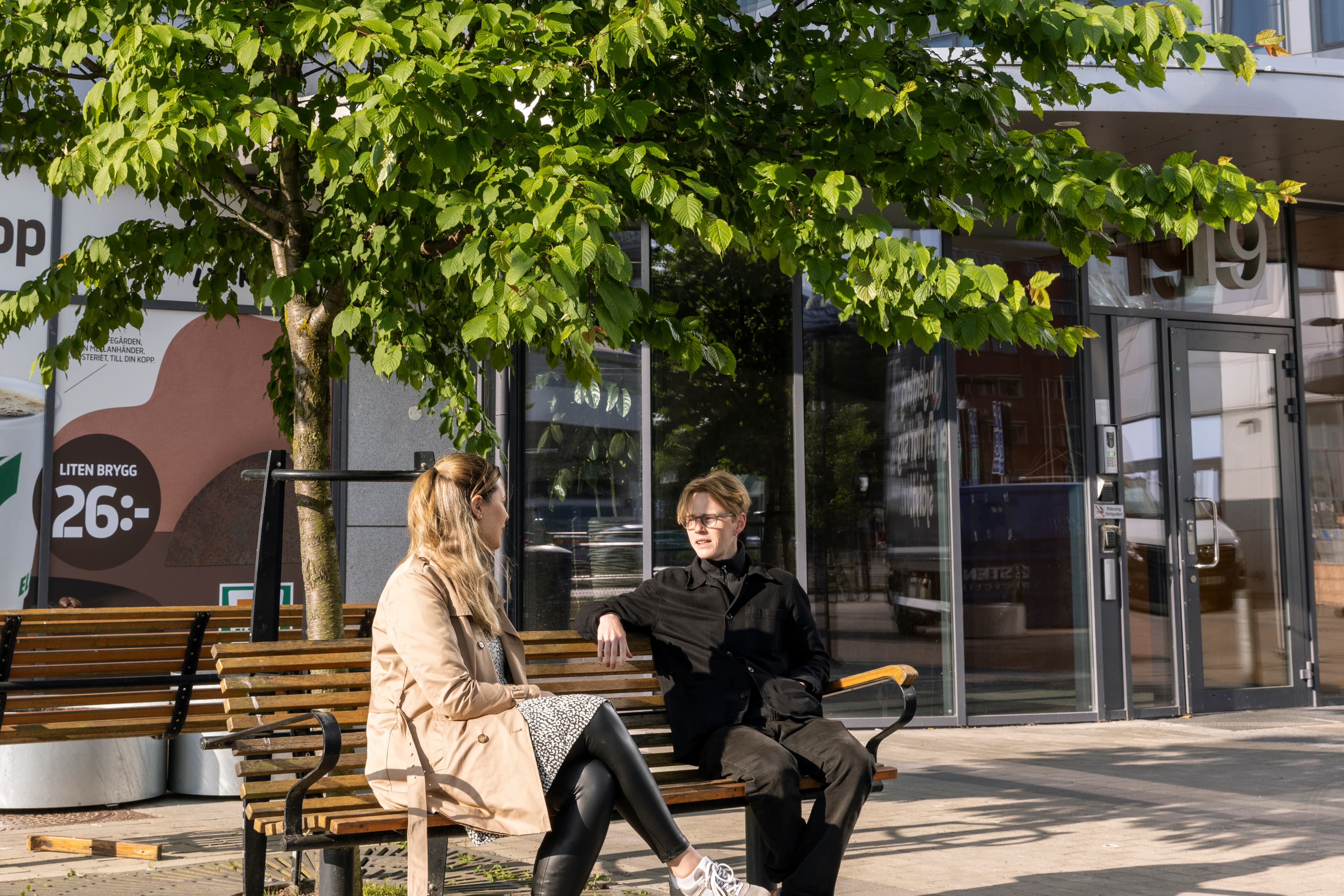 Två personer sitter på en bänk framför en byggnad.