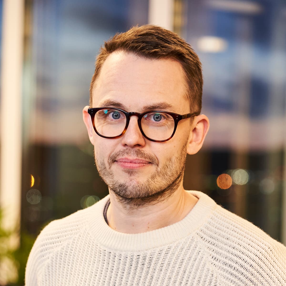 En man med glasögon står framför ett fönster.