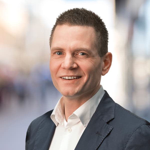 En man i kostym och vit skjorta ler.