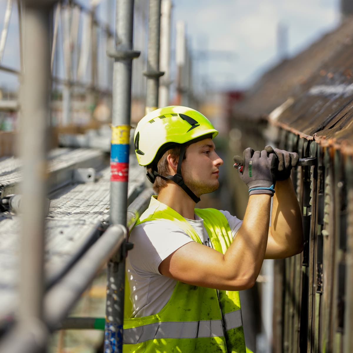 En man i skyddsväst och skyddshjälm arbetar på en byggnad.