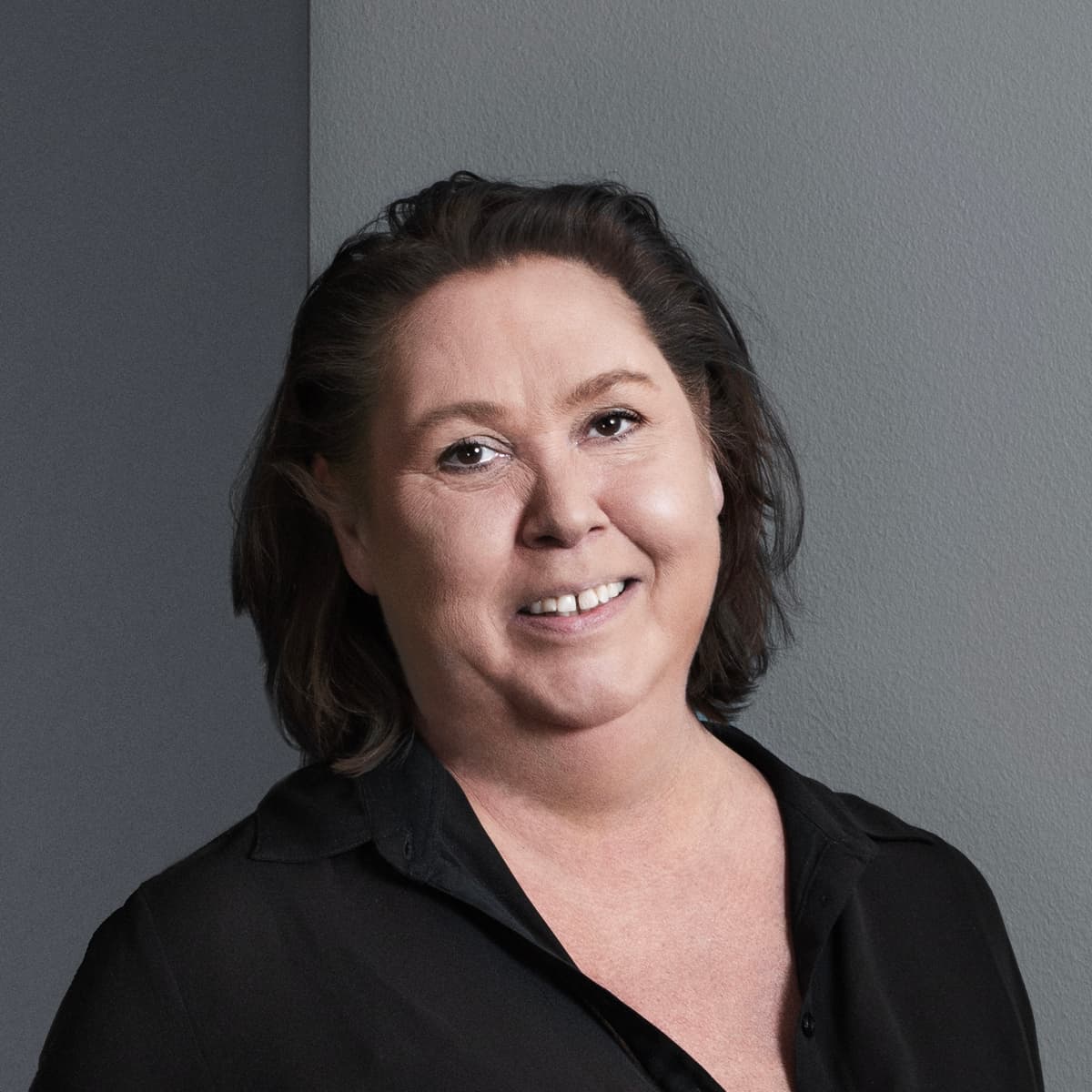 En kvinna i svart skjorta och svarta byxor lutar sig mot en vägg.