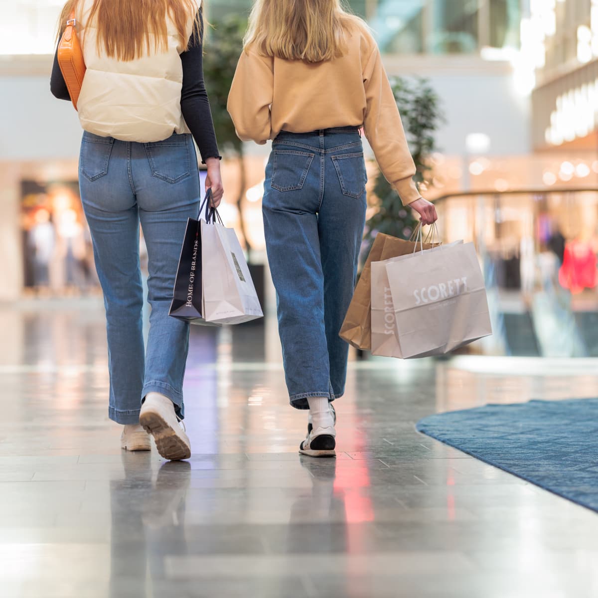 Två kvinnor går längs en korridor med shoppingkassar.