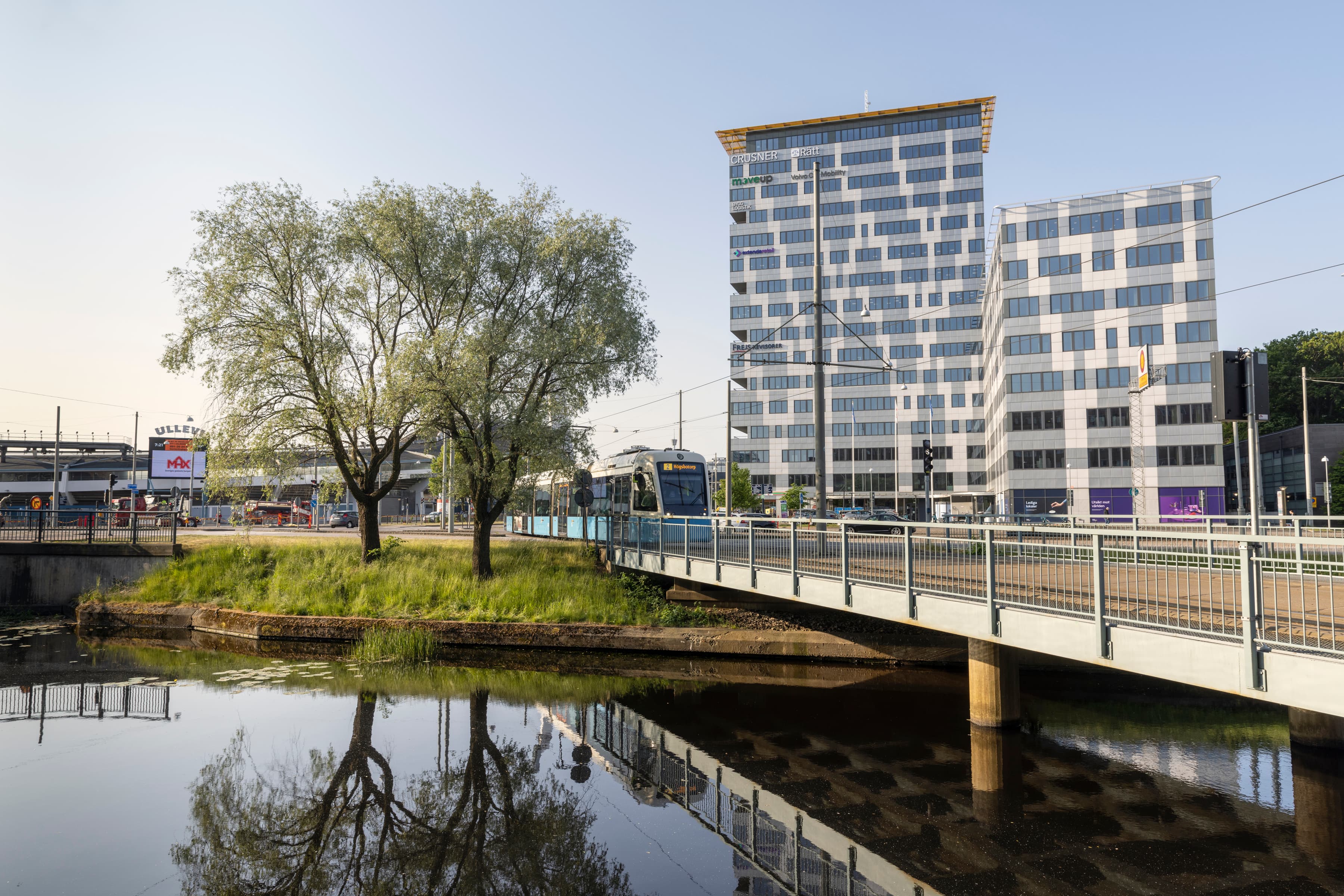 En bro över ett vattendrag med en byggnad i bakgrunden.