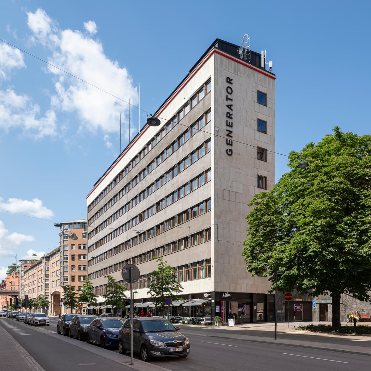 En stadsgata kantad av parkerade bilar och höga byggnader.