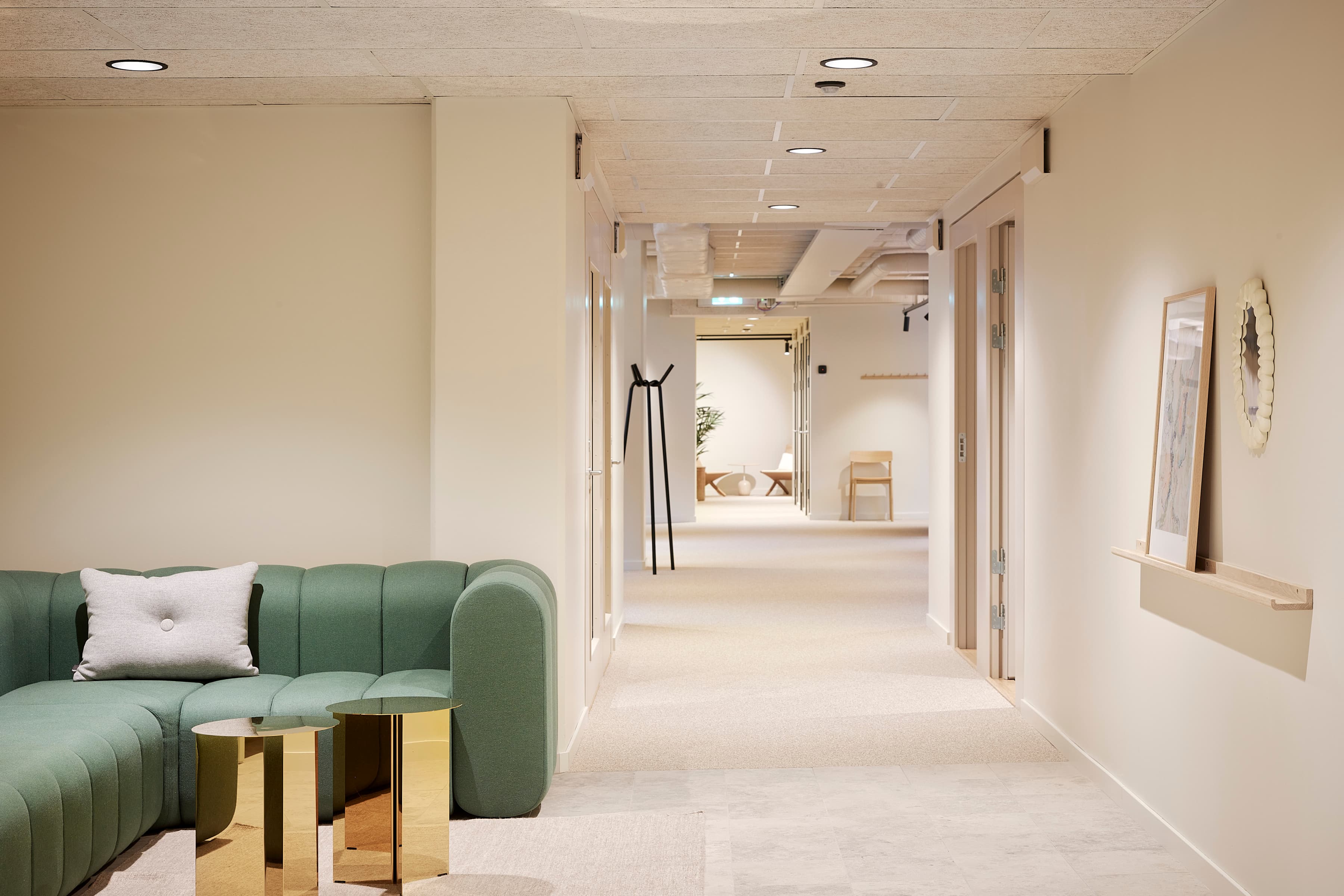 En grön soffa som sitter i ett vardagsrum bredvid en vit vägg.