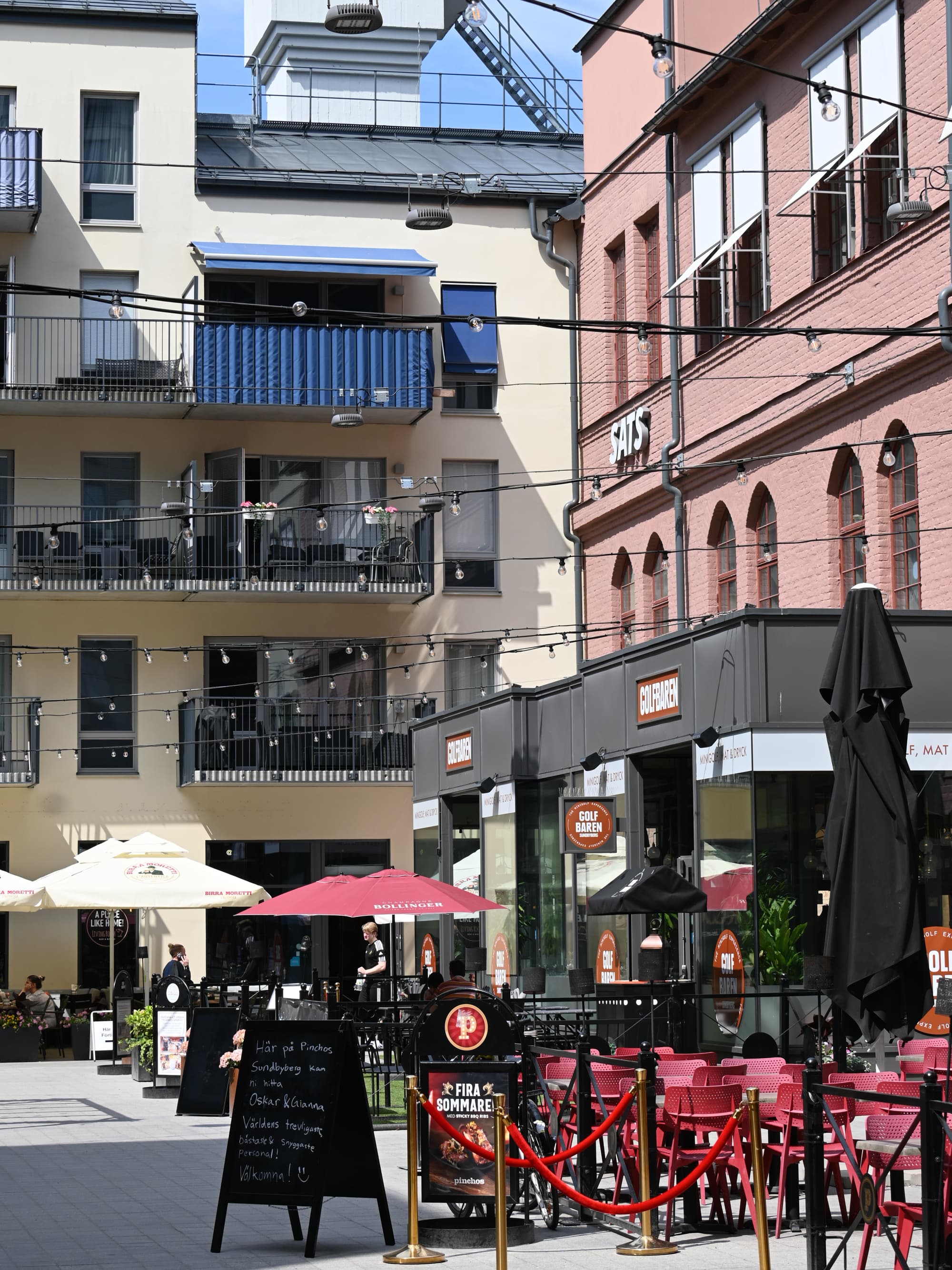 En trottoar med bord och parasoller framför en byggnad.