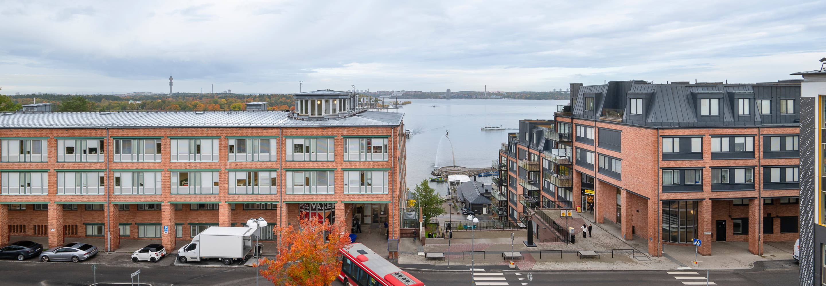 En röd buss kör längs en gata bredvid höga byggnader.