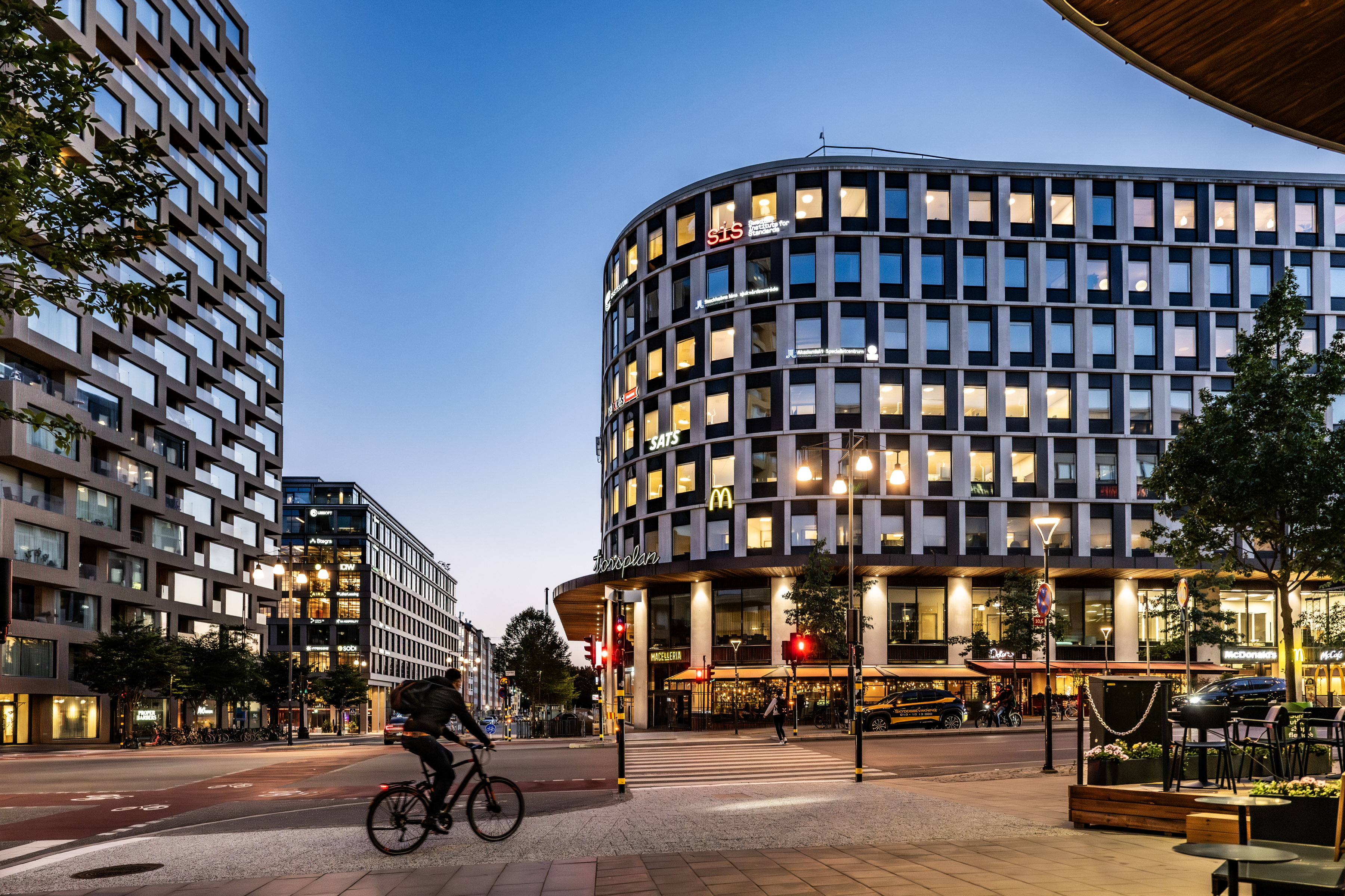 En man som cyklar längs en gata bredvid höga byggnader.