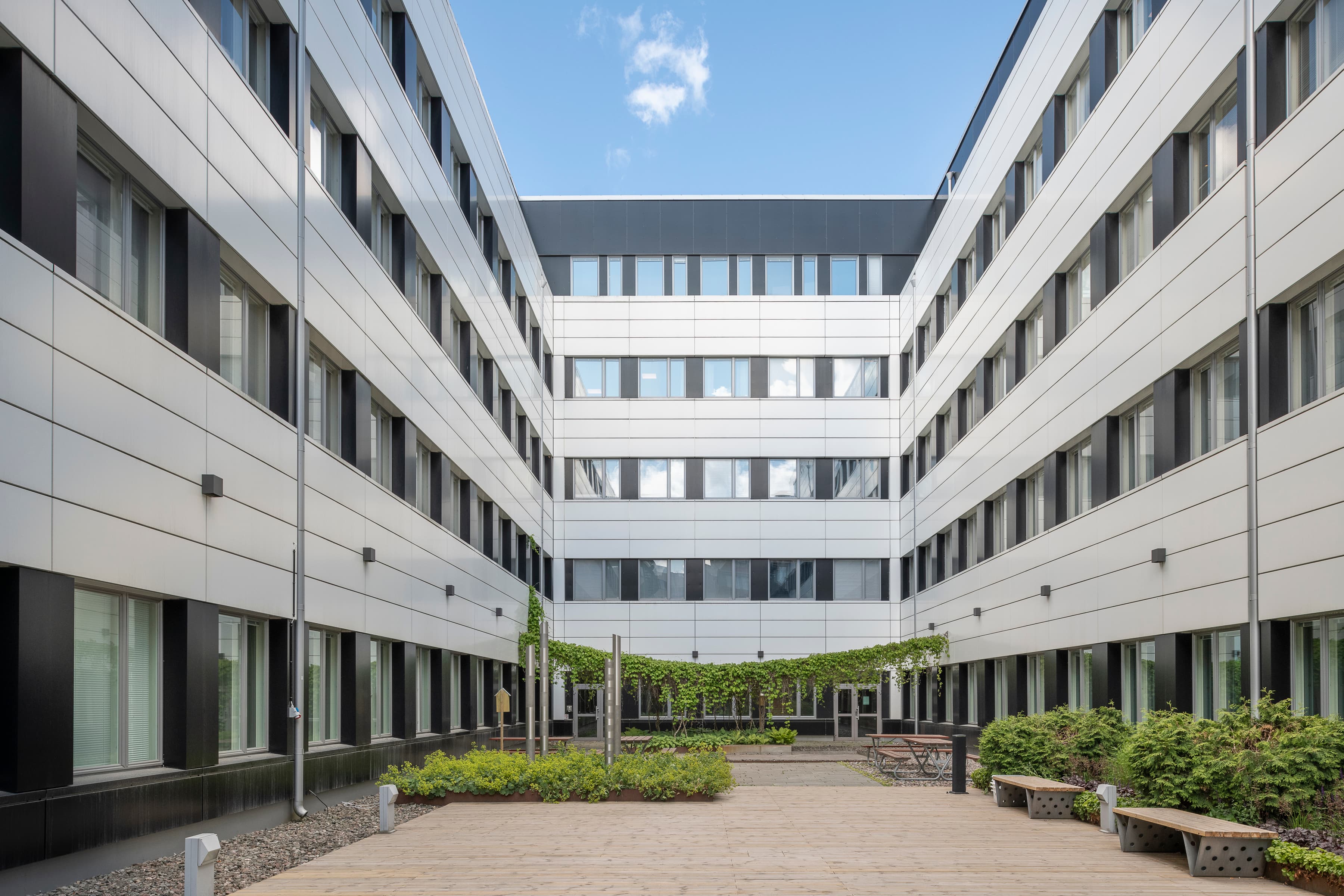 En innergård med bänkar och växter framför en byggnad.