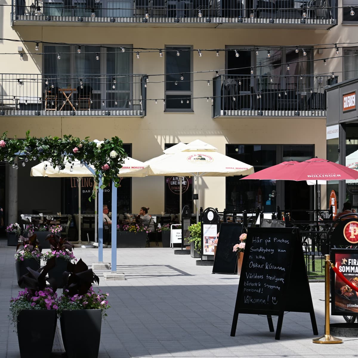 En trottoar med bord och parasoller framför en byggnad.