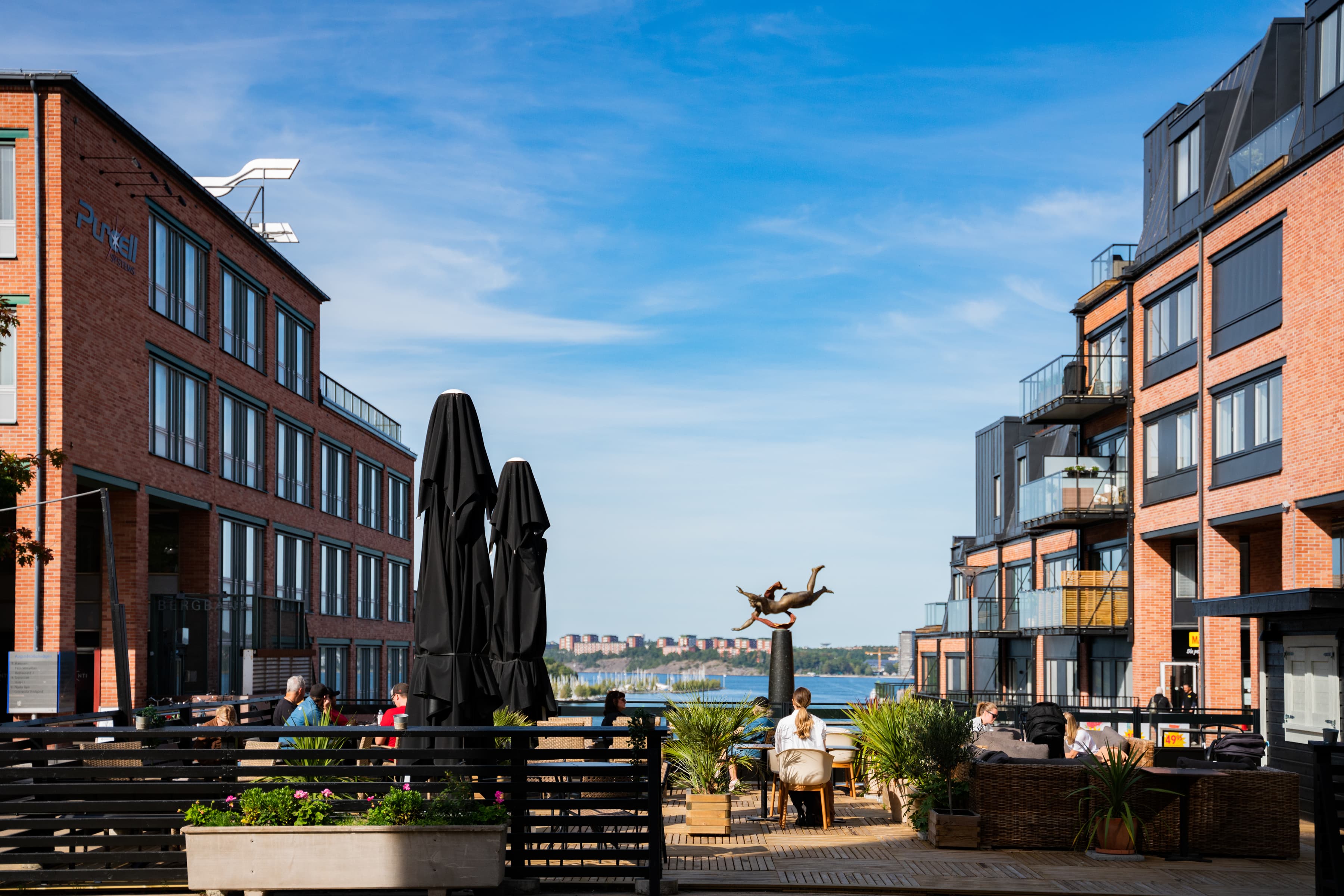 Några personer sitter på en bänk nära några byggnader.