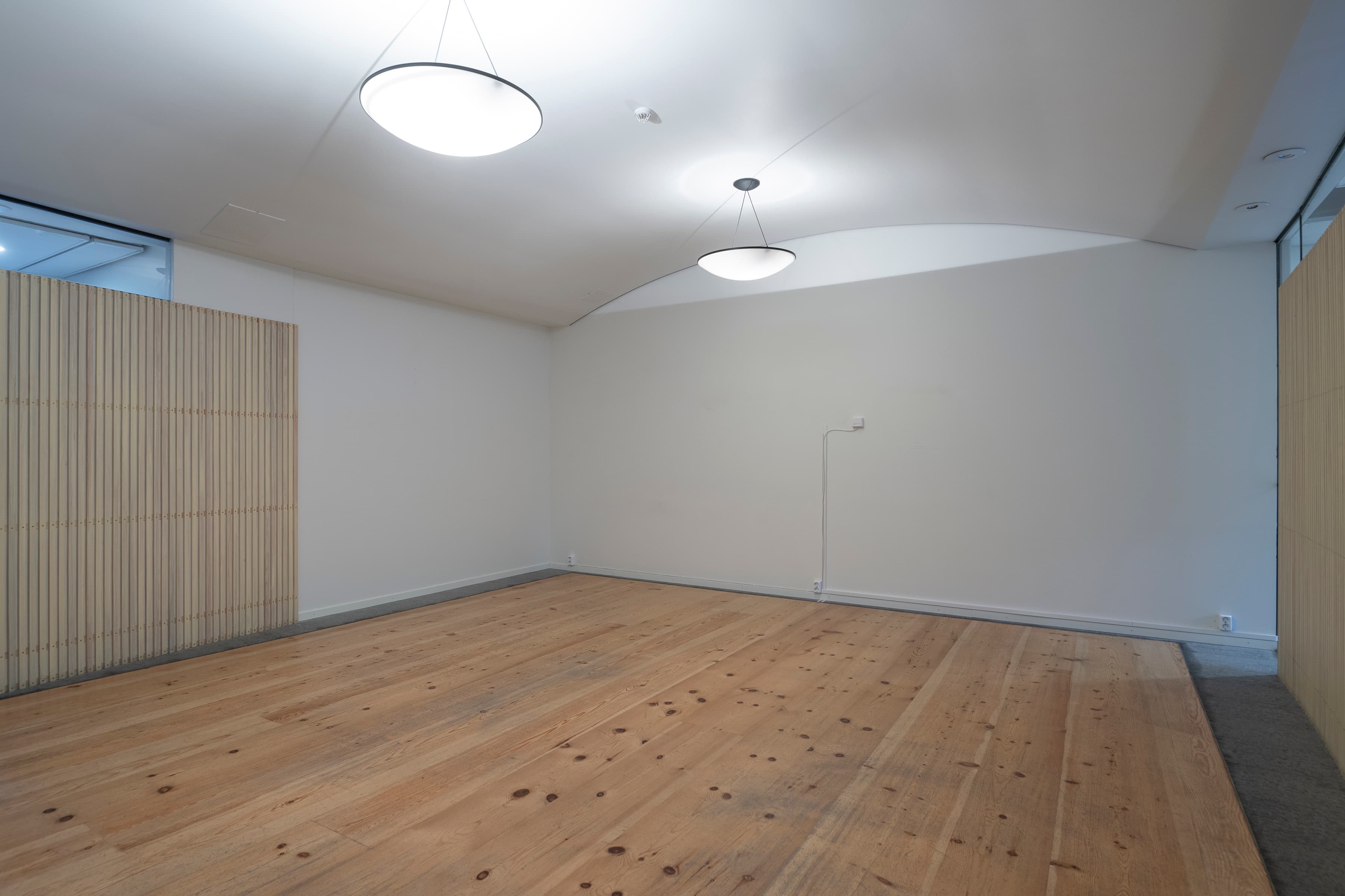 Ett tomt rum med trägolv och vita väggar.