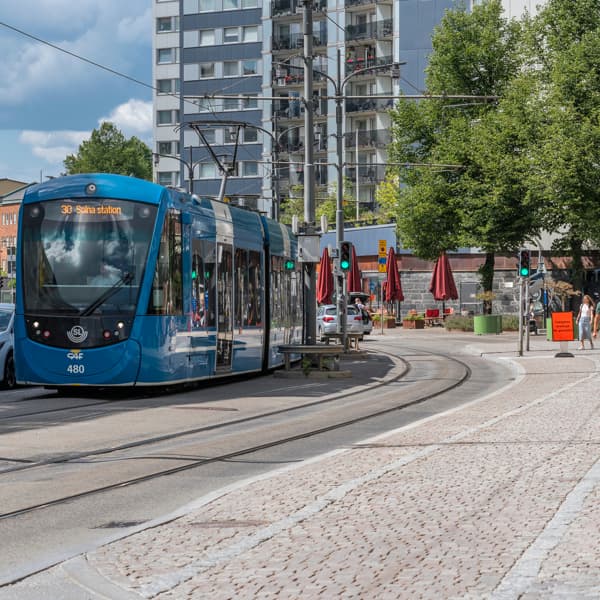 En blå spårvagn som kör längs en gata bredvid höga byggnader.