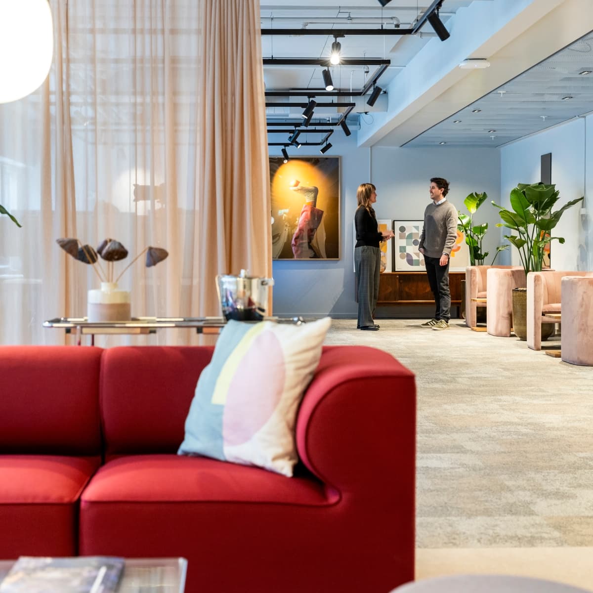 En röd soffa som sitter i ett vardagsrum under en målning.