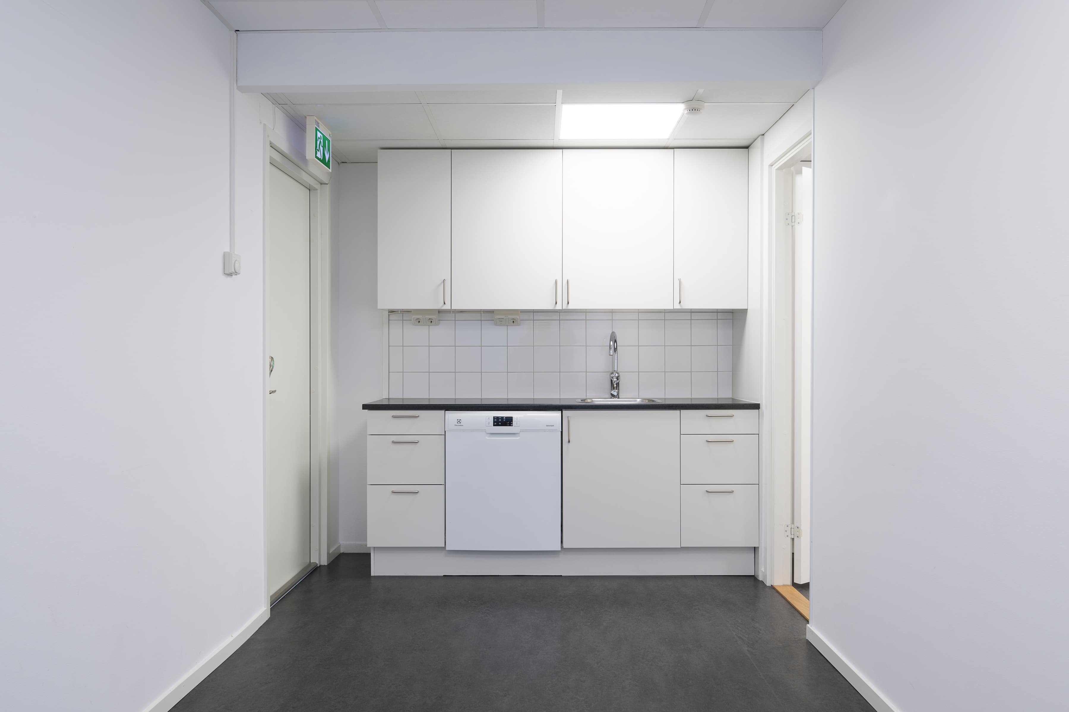 Ett tomt kök med vita skåp och svarta bänkskivor.