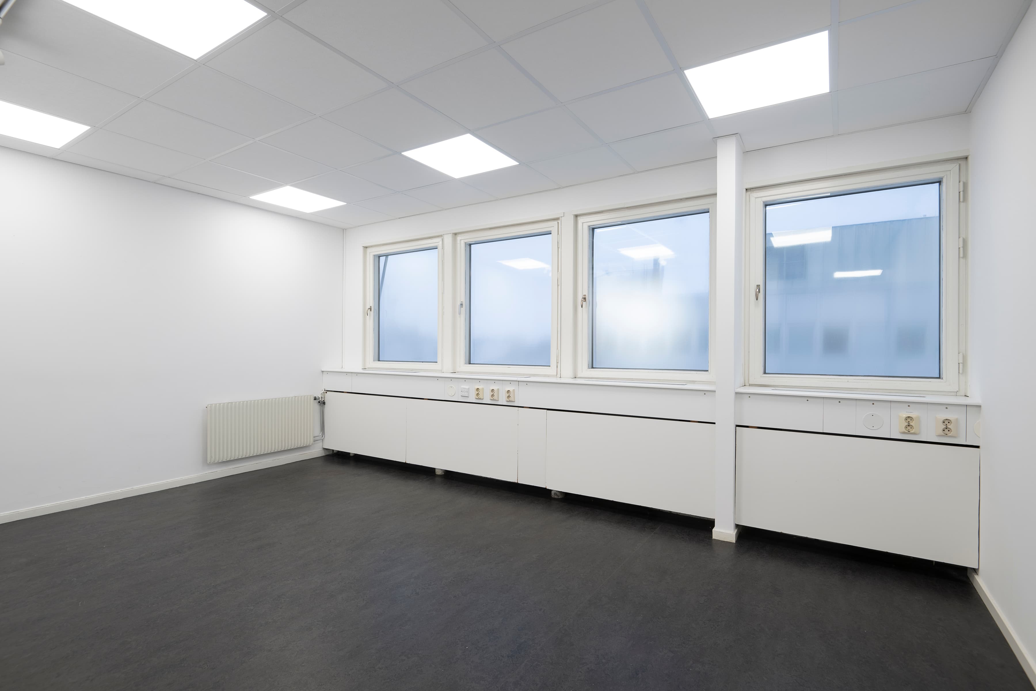 Ett tomt rum med tre fönster och en radiator.