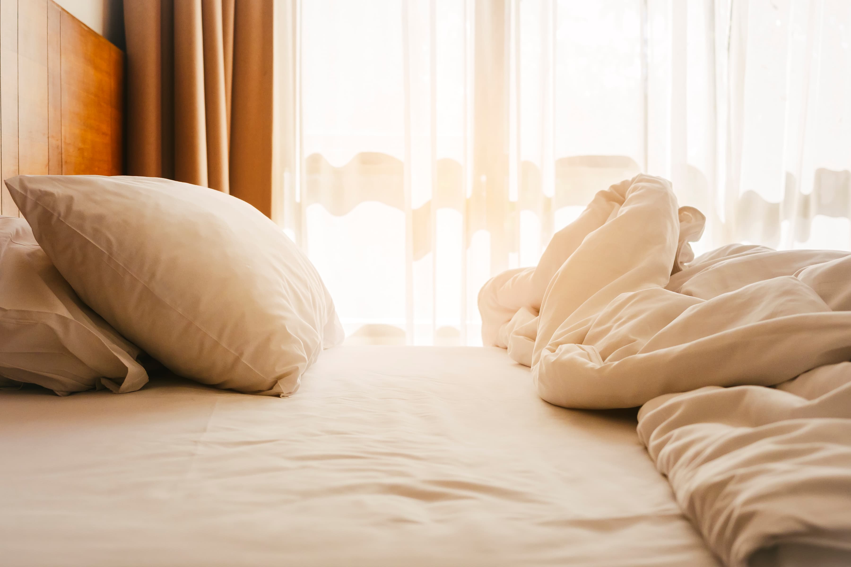 En obäddad säng med vita lakan och kuddar.