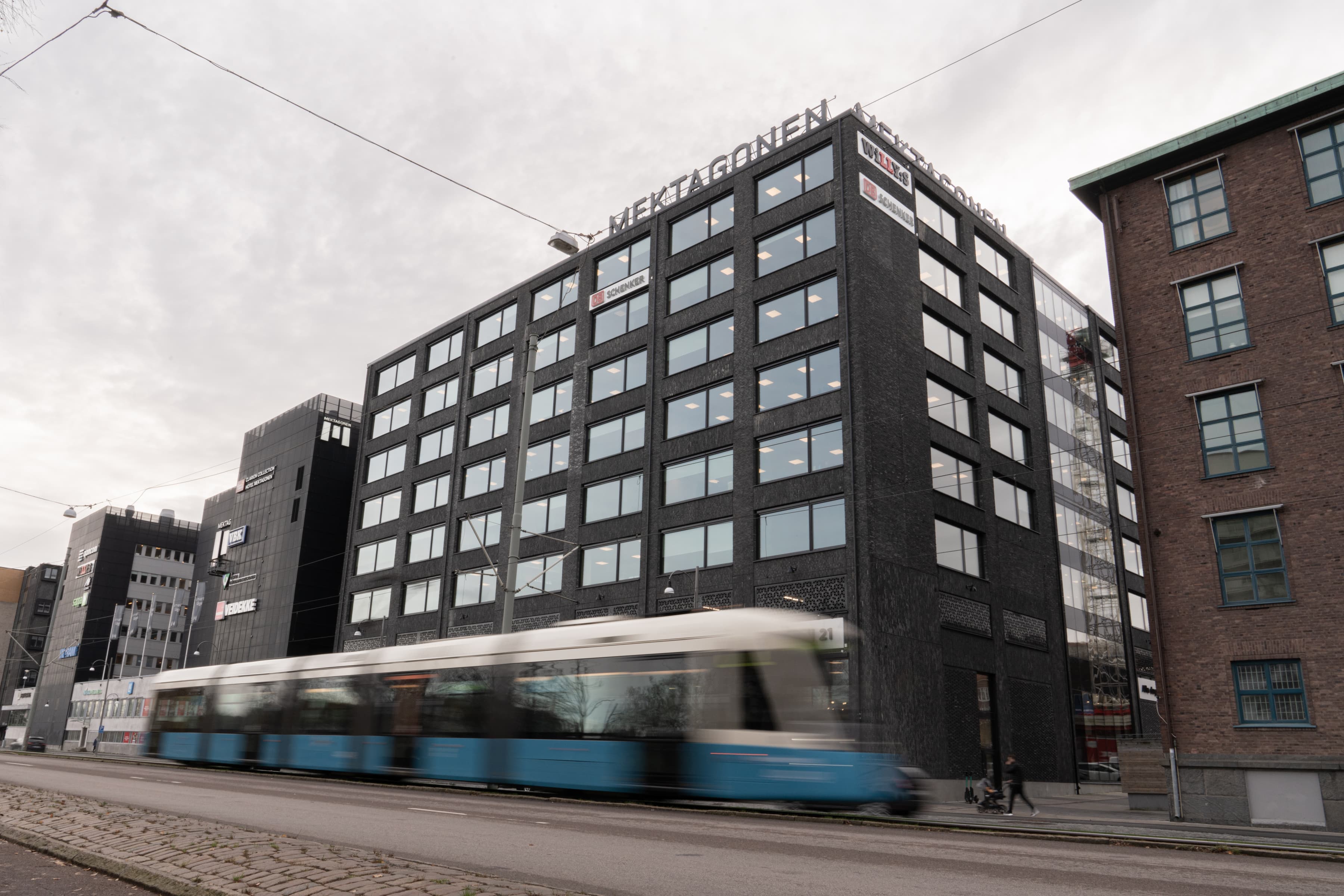 Ett blått och vitt tåg som passerar en hög byggnad.