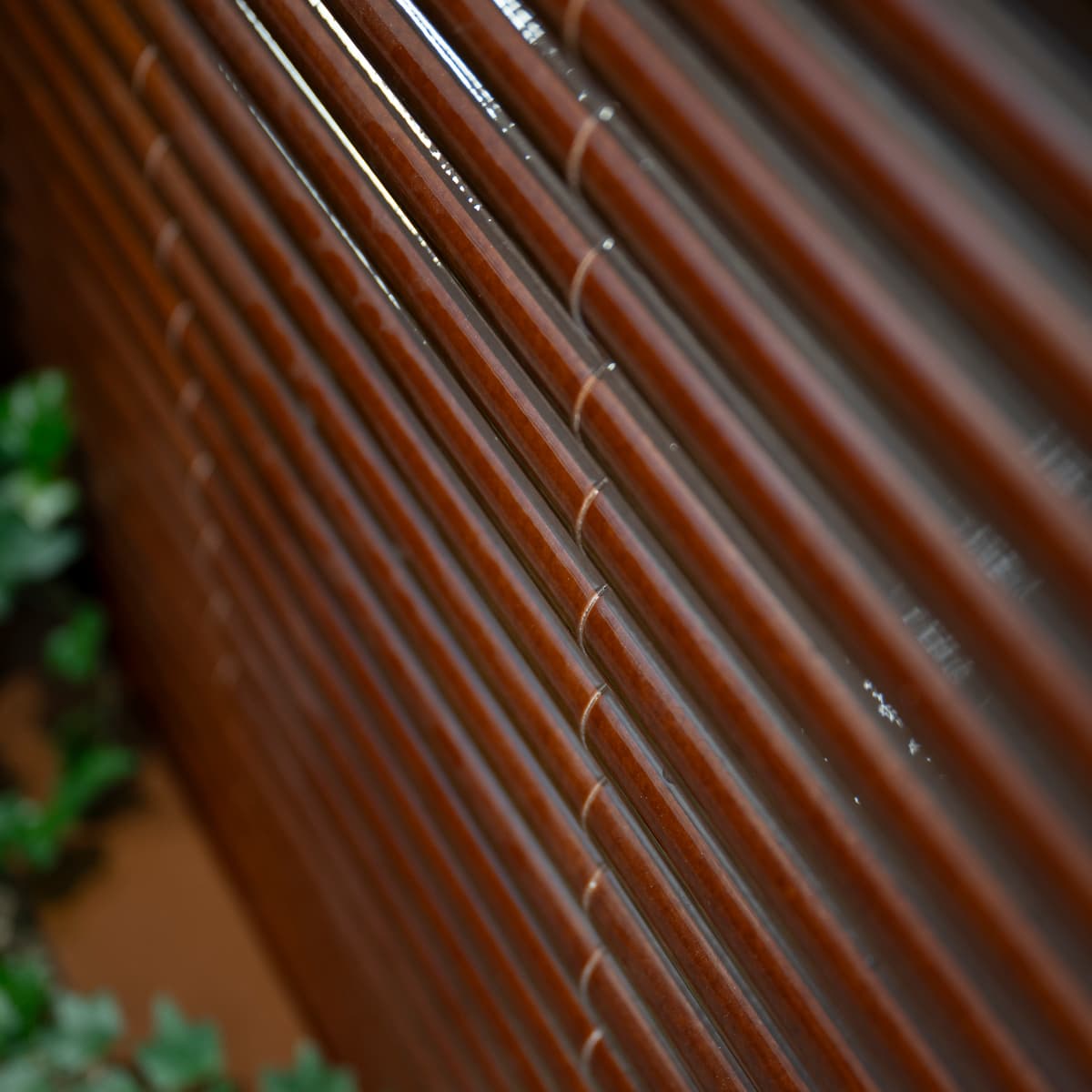 En närbild av en träpersienn med en växt i bakgrunden.