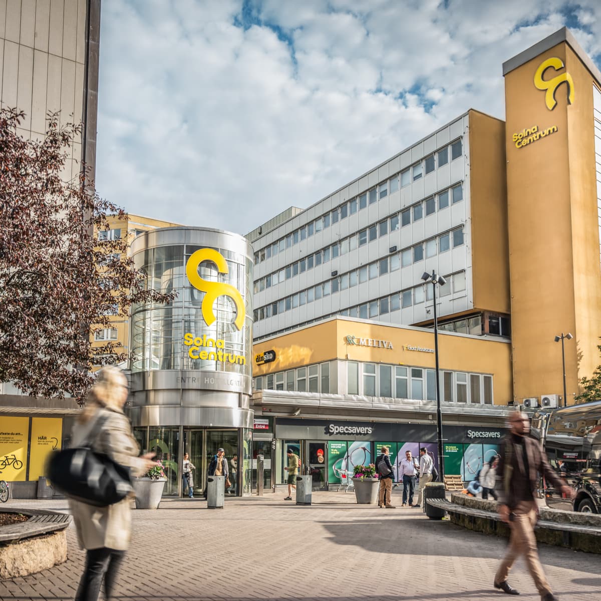 En grupp människor som går längs en gata bredvid höga byggnader.