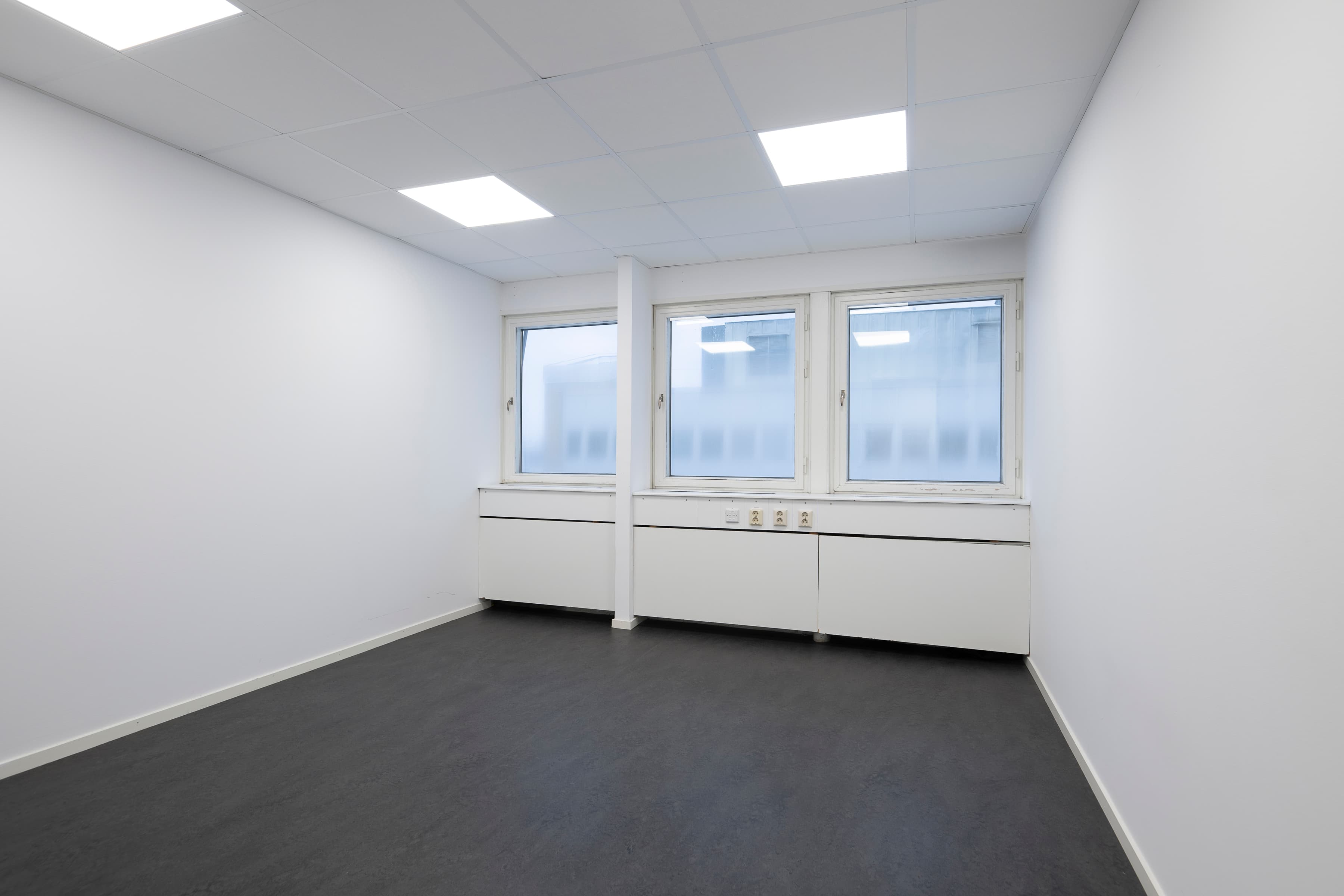 Ett tomt rum med tre fönster och en radiator.