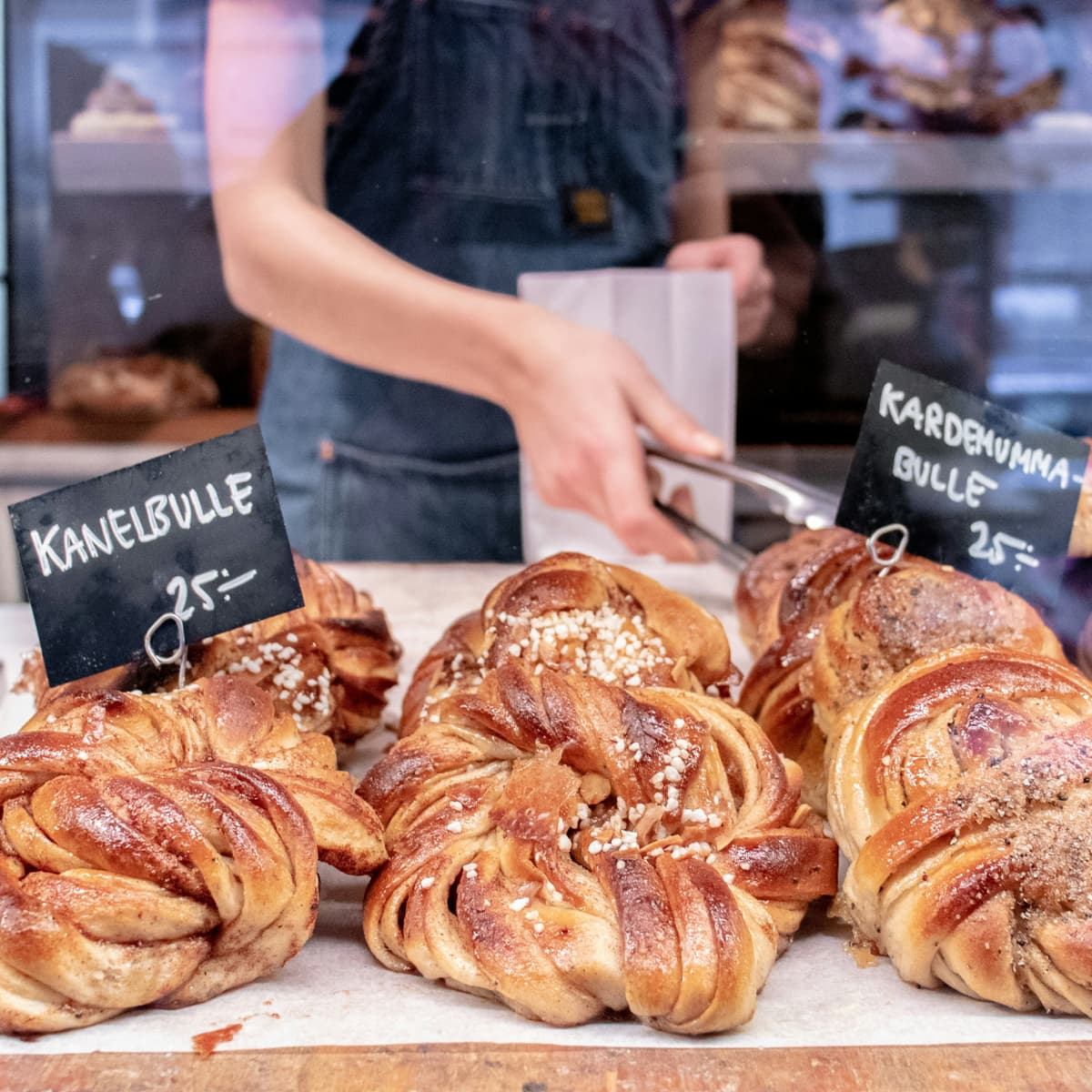 En person som står bakom en utställning av bakverk.