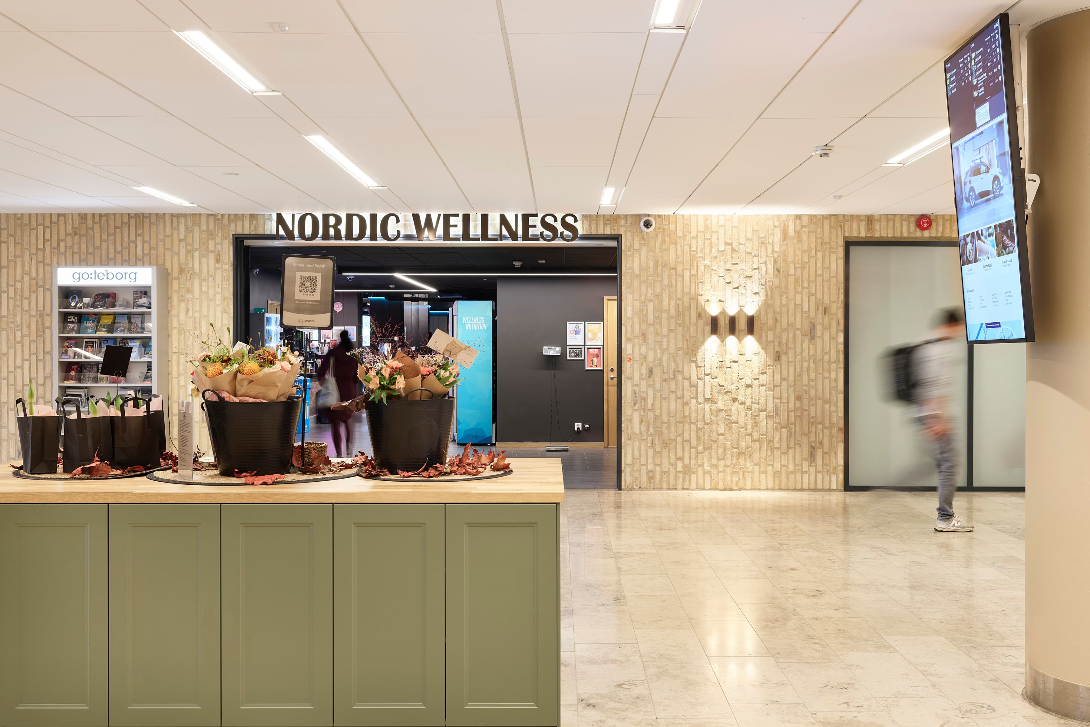 En person som går förbi en butiksfasad med blommor på disken.